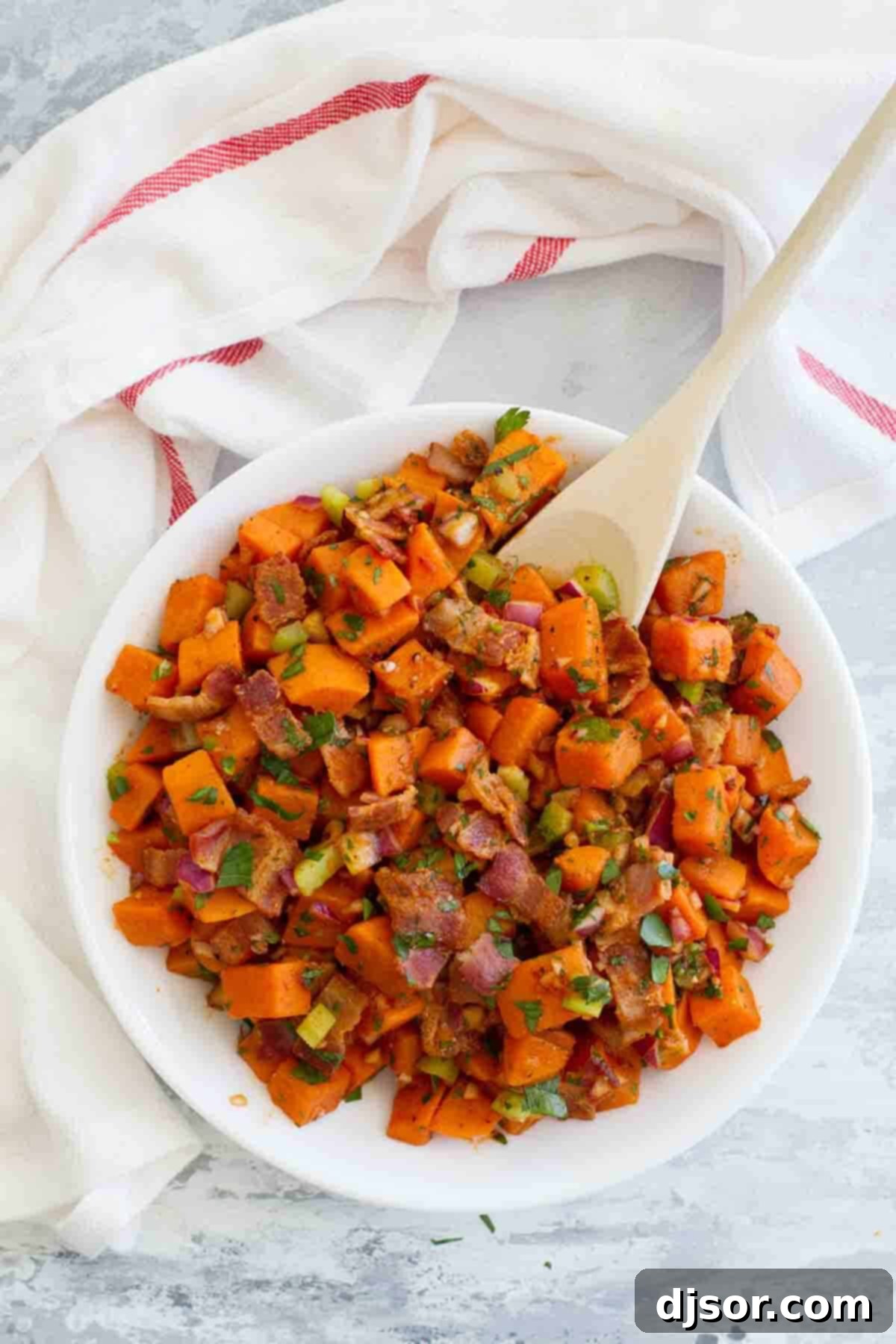 Generous Portion of Sweet Potato Salad A large white bowl filled with Sweet Potato Salad with Bacon, accompanied by a wooden serving spoon, set on a wooden surface.