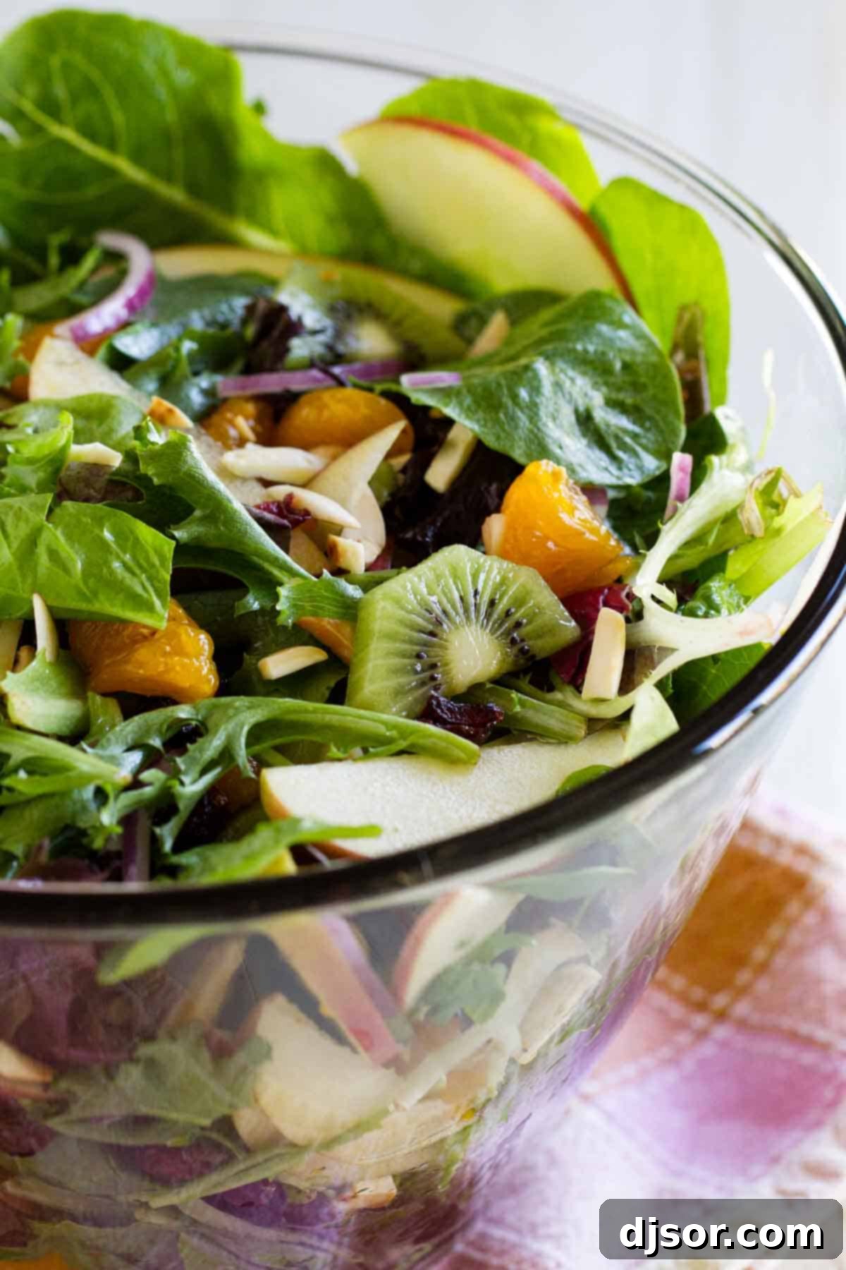 Steph's Radiant Summer Salad 3 A large glass bowl filled with Steph's Summer Salad, prominently featuring slices of kiwi and mandarin oranges amidst the greens.