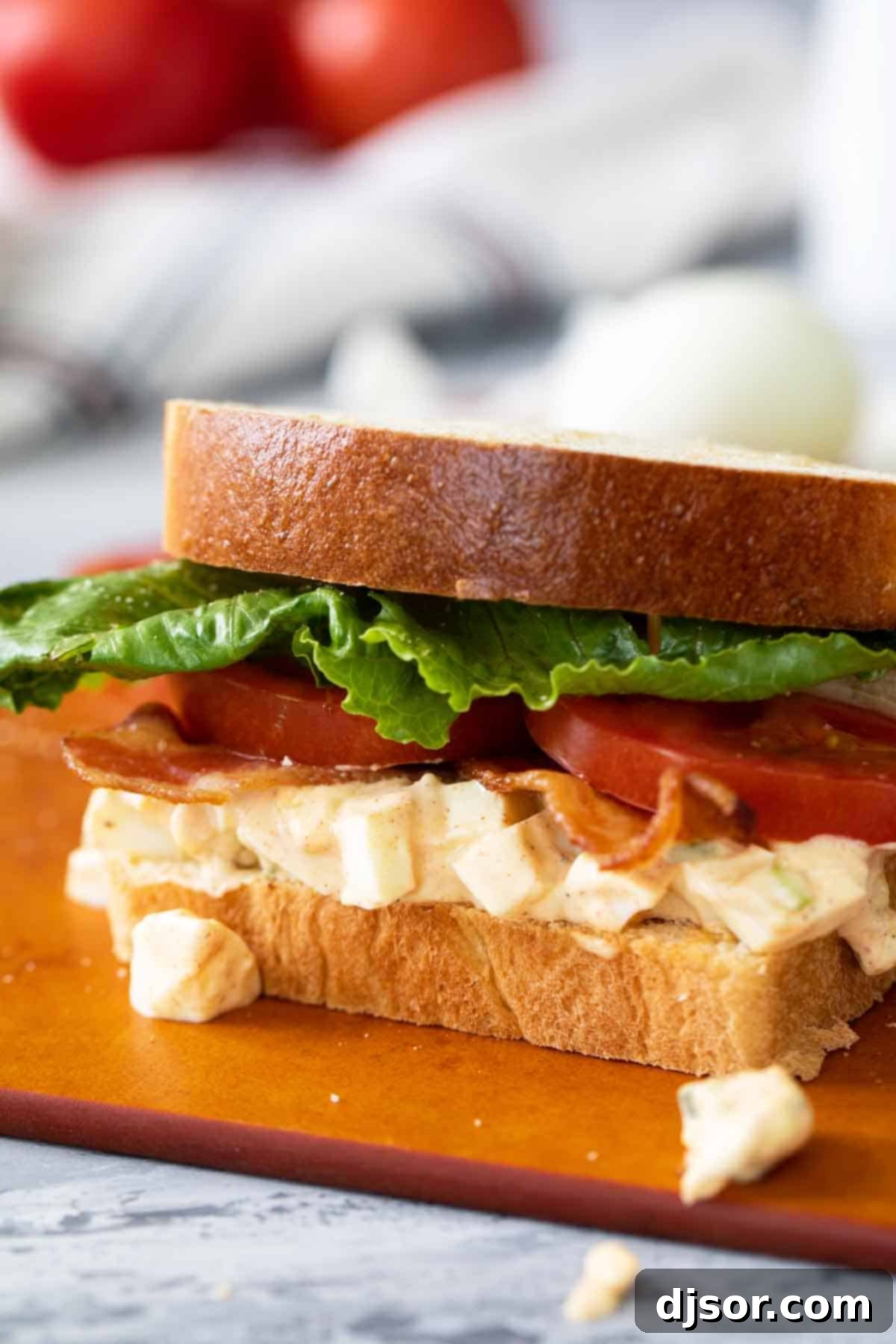 A freshly made Egg Salad BLT, cut in half, showcasing layers of egg salad, bacon, lettuce, and tomato, on toasted bread.