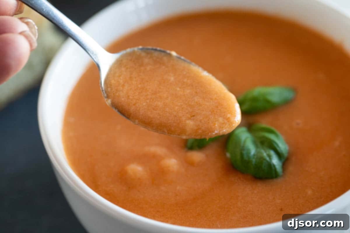 An easy slow cooker soup recipe, this Tomato Basil Soup is full of tomato flavor, is super creamy, and is easily a family favorite! A spoon scooping up creamy tomato basil soup, showing its rich texture.