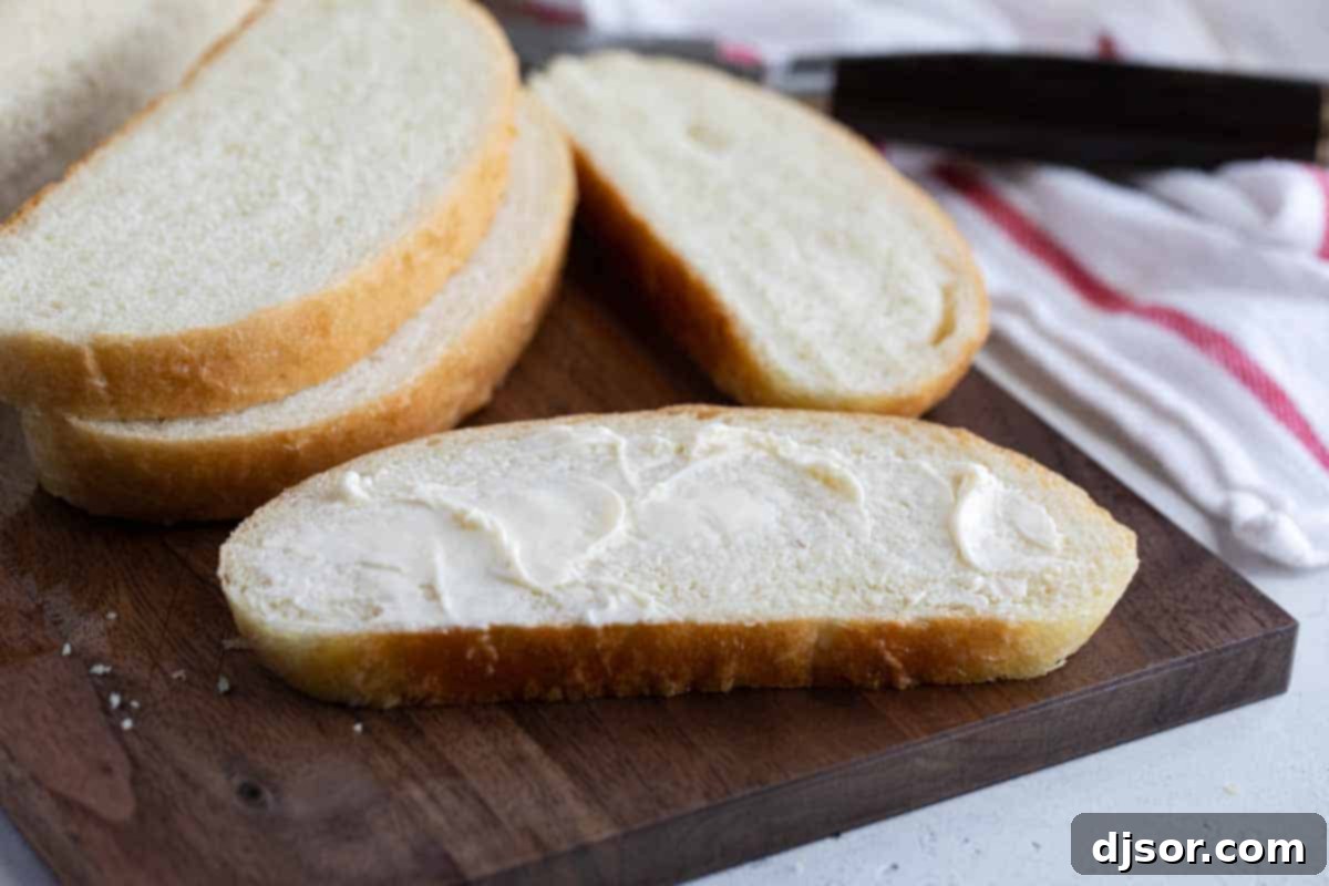 sliced loaf of Peasant Bread with butter on one slice, showcasing its soft interior and golden crust