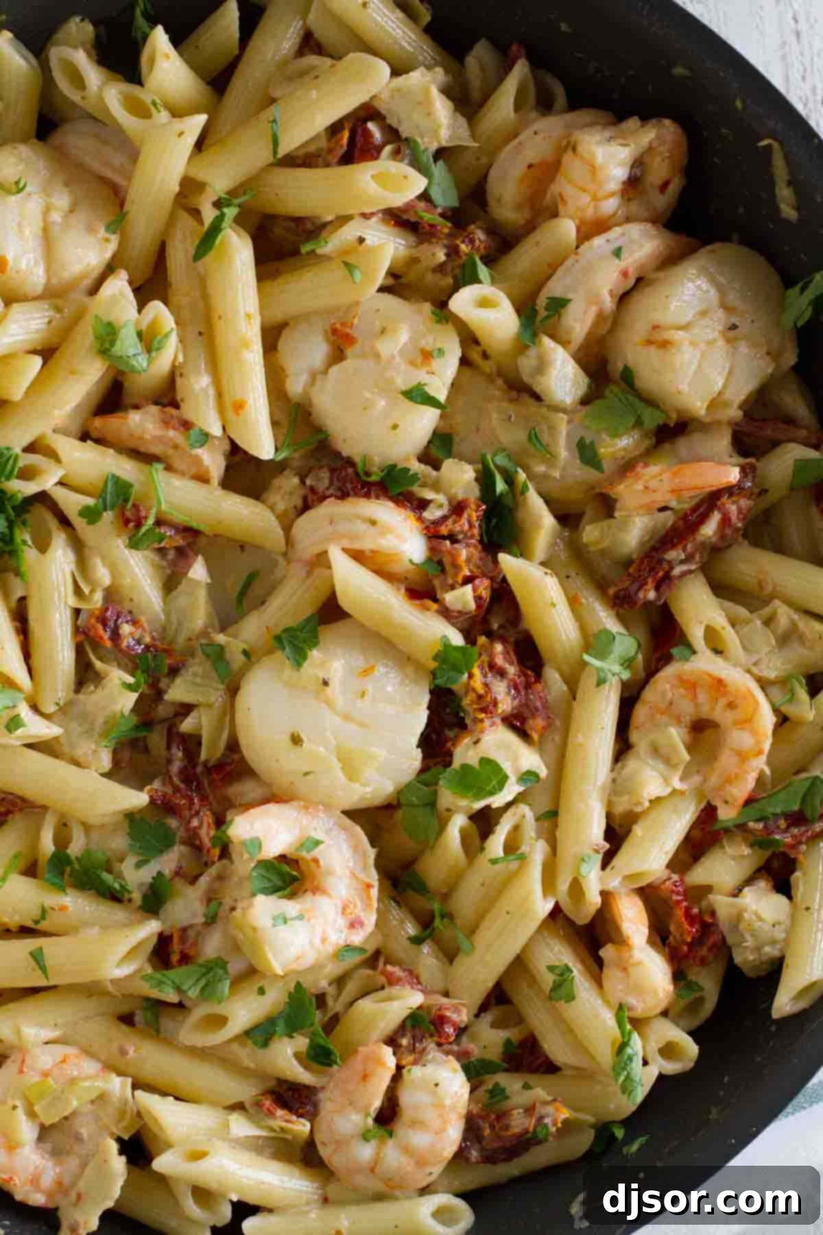 Key West Penne: Shrimp, Scallops, Sun-Dried Tomatoes & Artichoke Hearts Pasta A large pan brimming with Key West Penne, showcasing pasta, plump shrimp, tender scallops, and vibrant sun-dried tomatoes.