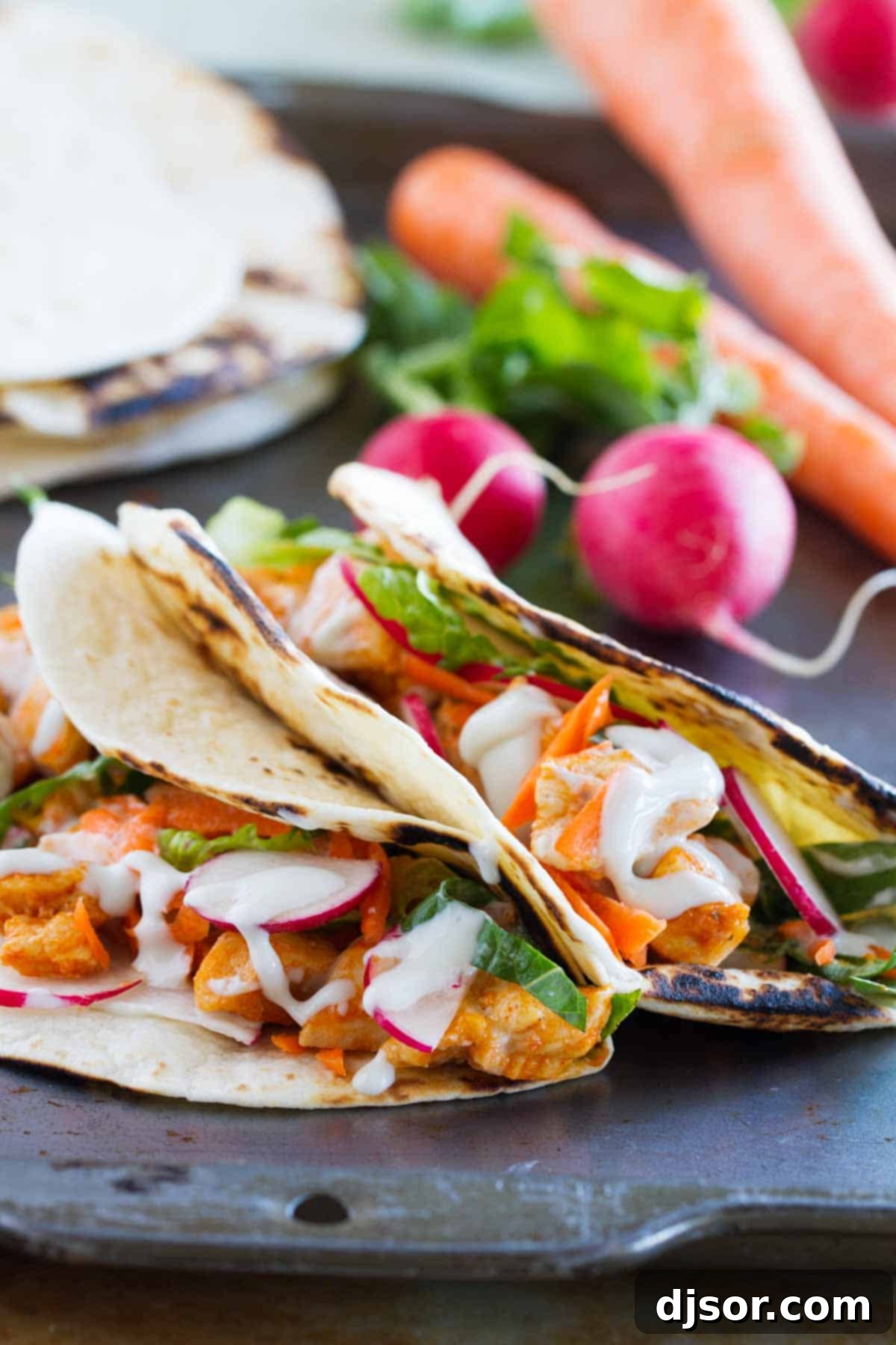 Buffalo Chicken Tacos made with buffalo chicken, lettuce, radishes, and blue cheese sauce. A close up shot of a taco filled with chicken and fresh toppings.