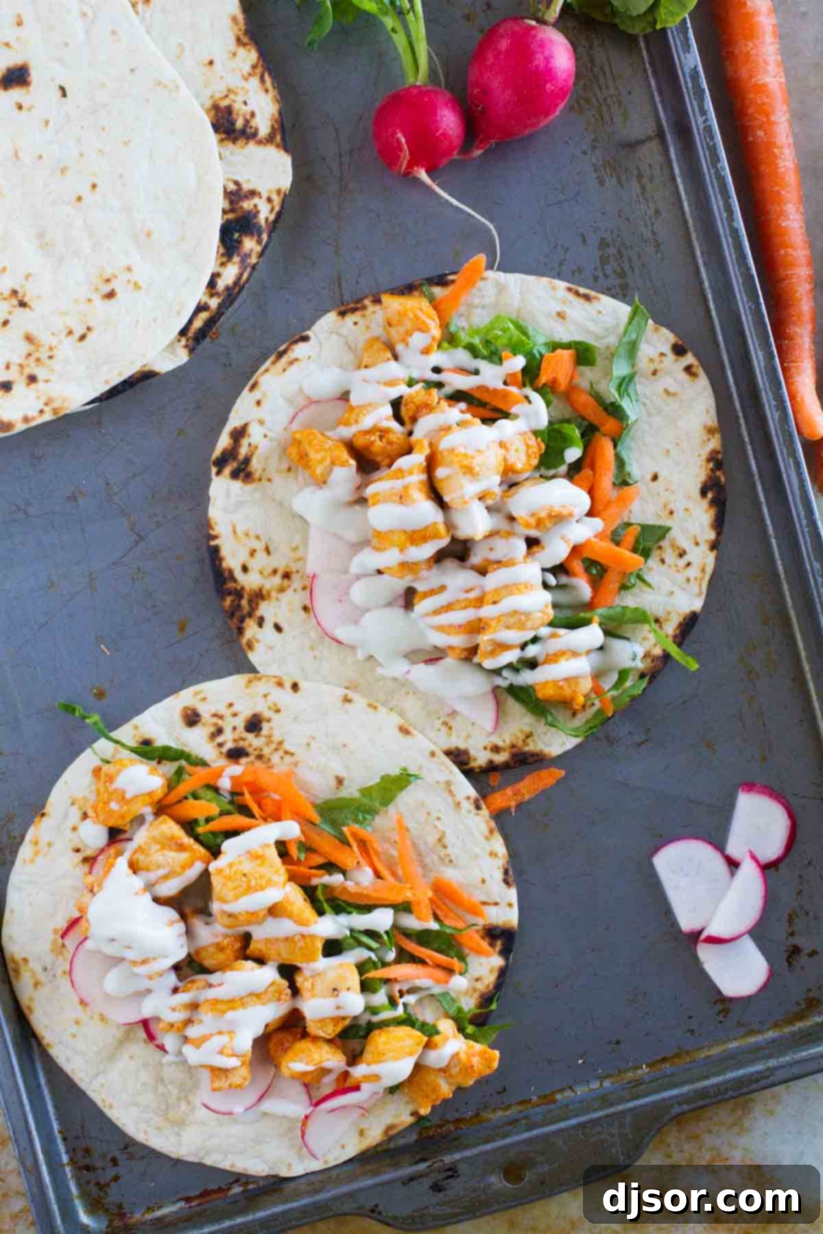 Buffalo chicken tacos open on a baking sheet, showing the filling before folding.