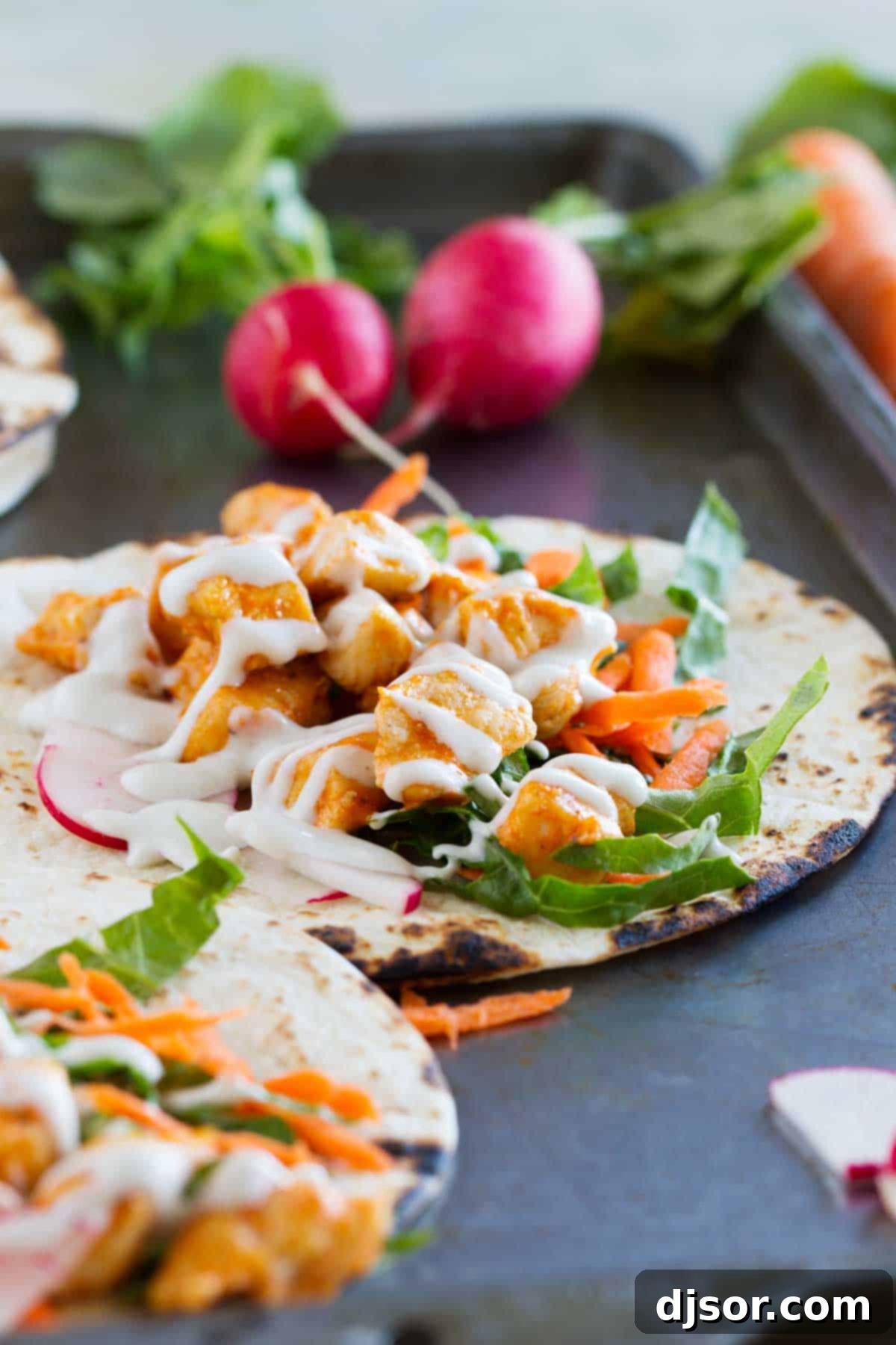 Tortillas filled with buffalo chicken and taco toppings, ready to be folded and served.