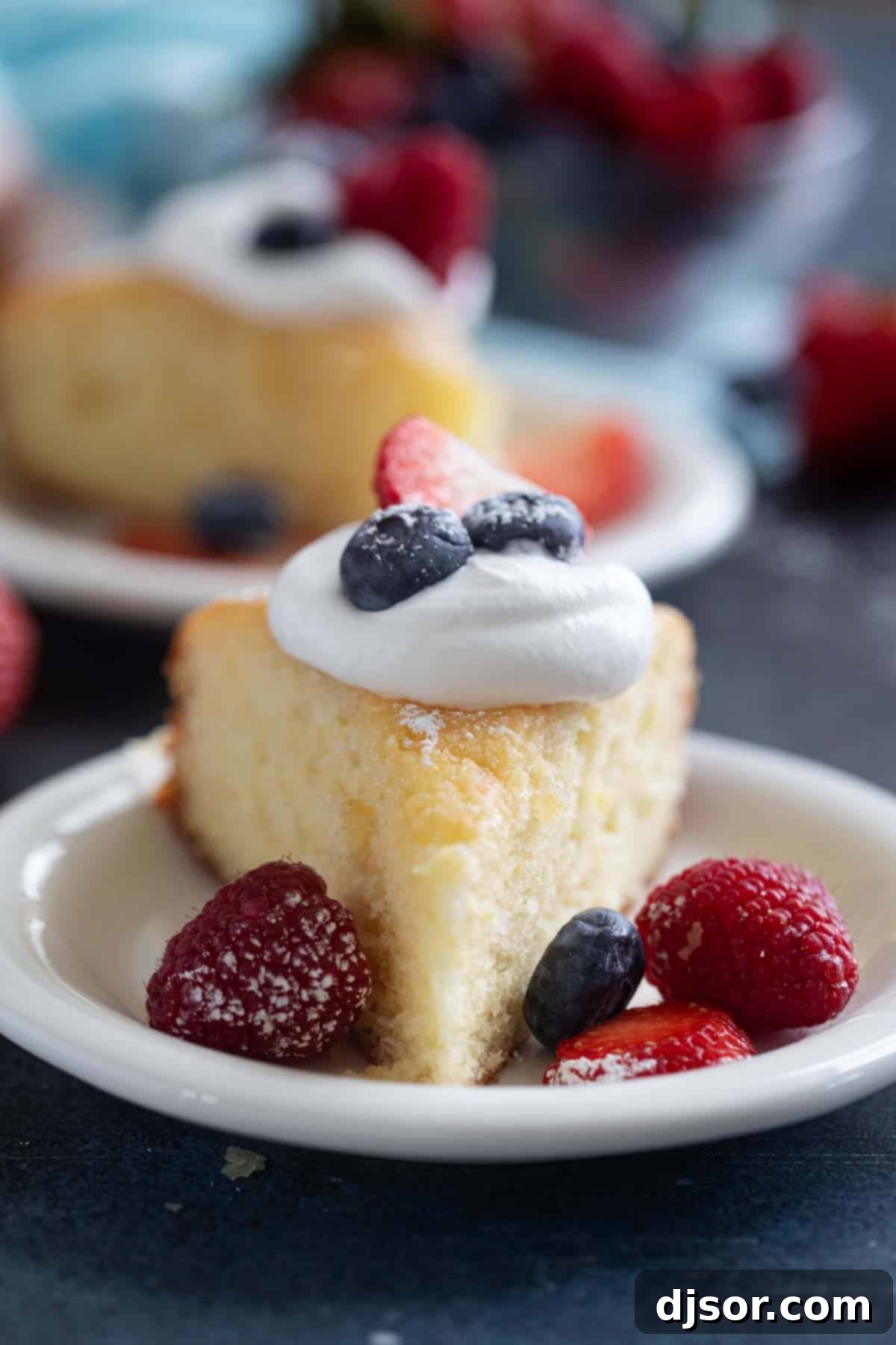 A close-up of a single slice of moist Lemon Yogurt Cake, beautifully garnished with a swirl of whipped cream and a sprinkle of fresh mixed berries.