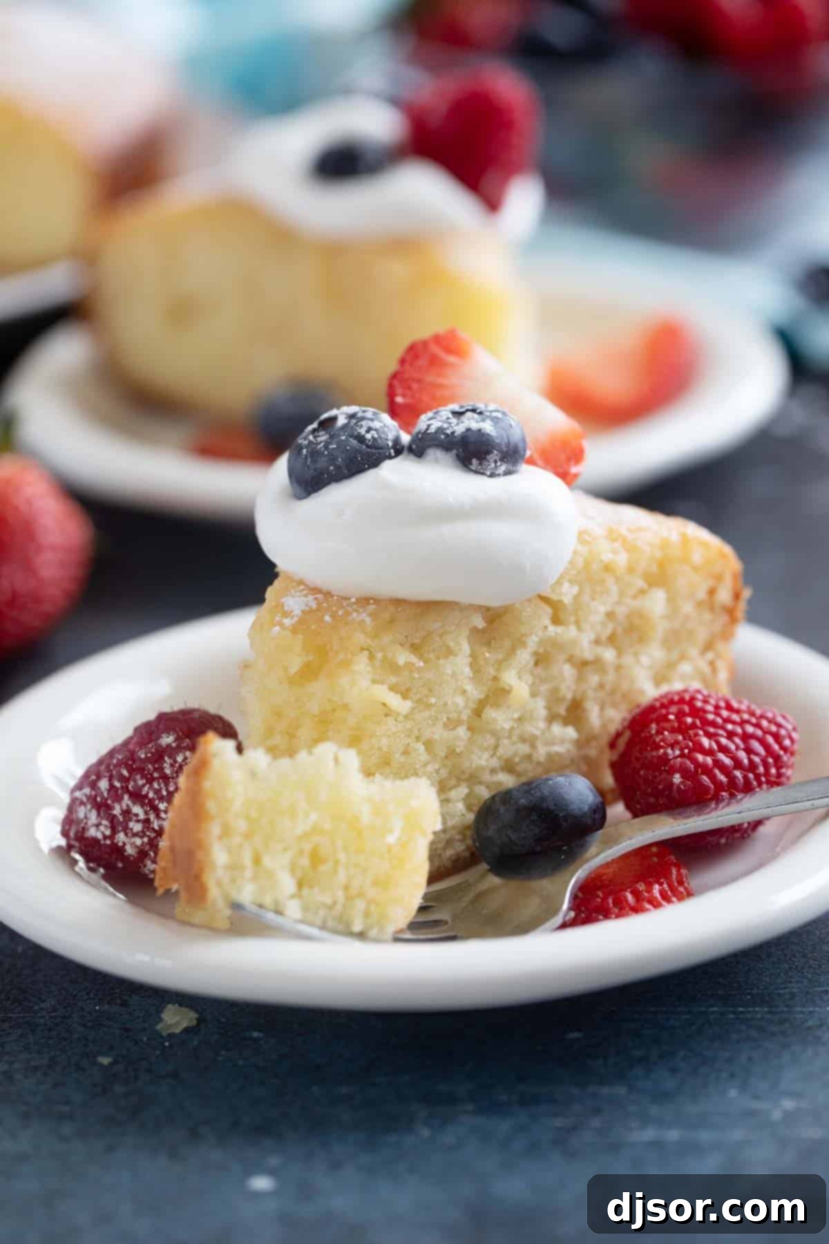 A close-up shot of a slice of Lemon Yogurt Cake on a plate, with a fork holding a perfect bite of the moist cake, highlighting its delicate texture.
