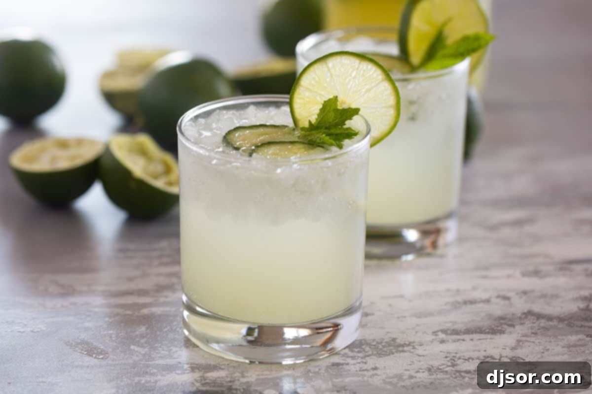Cucumber Lime Chill 2 Two glasses of cucumber limeade with fresh limes, garnished with cucumber slices and mint leaves on a rustic wooden surface.