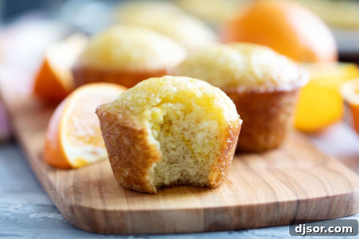 These Orange Muffins are moist and flavorful, slightly sweet with an orange simple syrup for the perfect finishing touch. A perfectly baked Orange Muffin made with fresh orange juice, with a section gently pulled apart to reveal its moist interior.