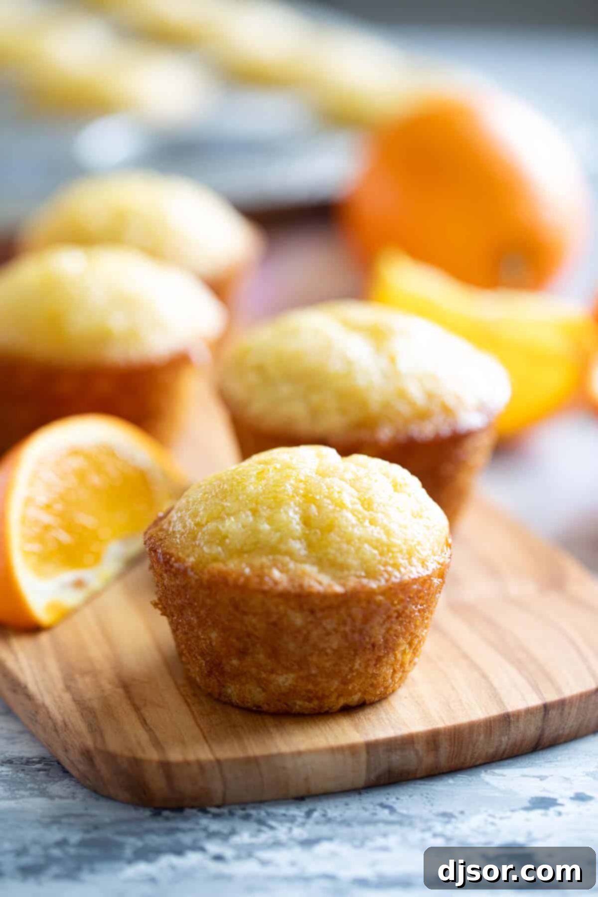 These Orange Muffins are moist and flavorful, slightly sweet with an orange simple syrup for the perfect finishing touch. Freshly baked Orange Muffins, glistening with a generous coating of orange simple syrup, arranged invitingly on a rustic wooden board.