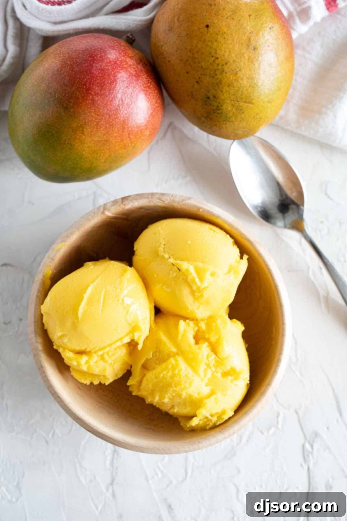 Fresh mangoes and lime juice come together to make a perfectly tropical Mango Sorbet. Mango sorbet in a bowl with fresh mangoes behind