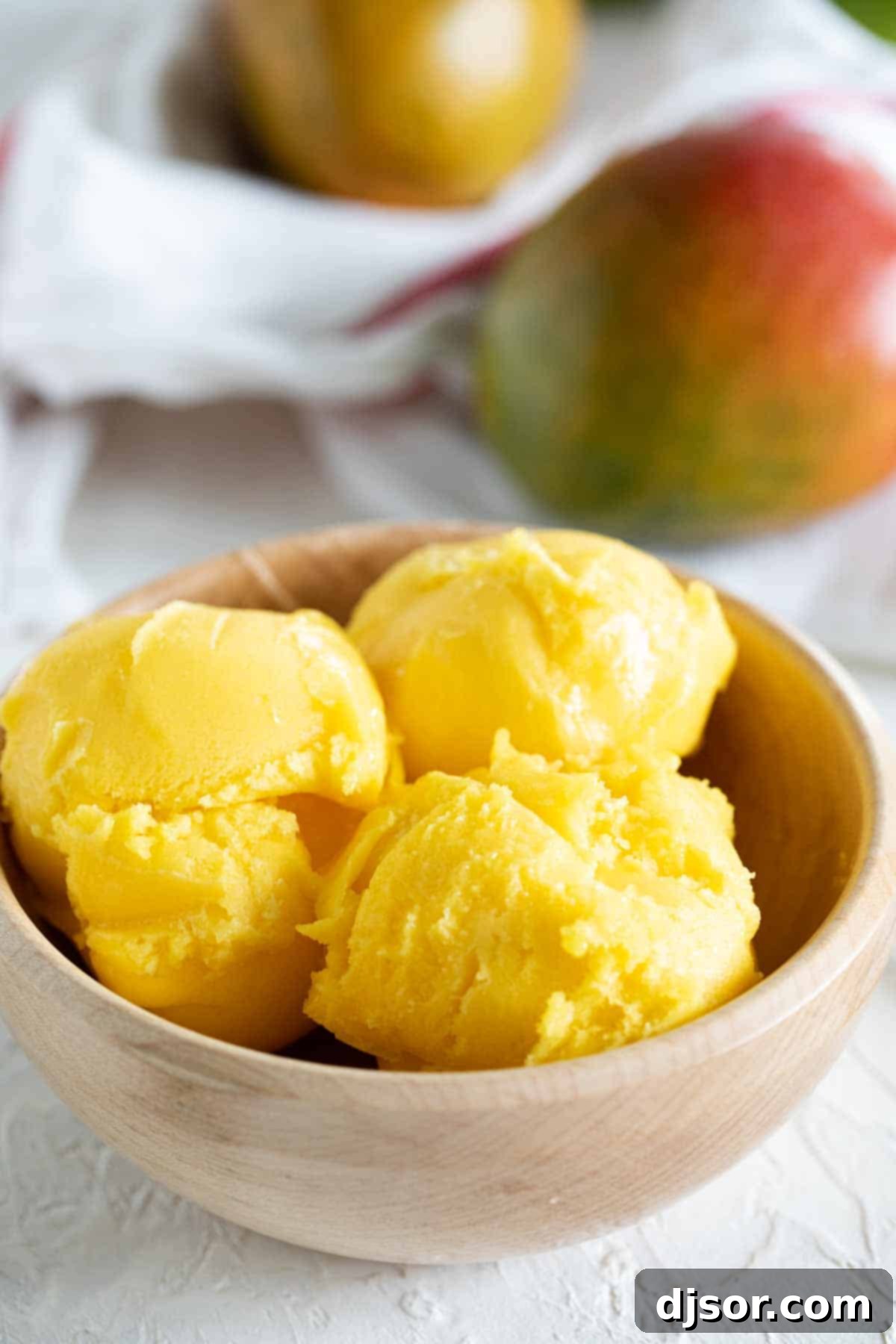 Fresh mangoes and lime juice come together to make a perfectly tropical Mango Sorbet. Wooden bowl with three scoops of Mango Sorbet