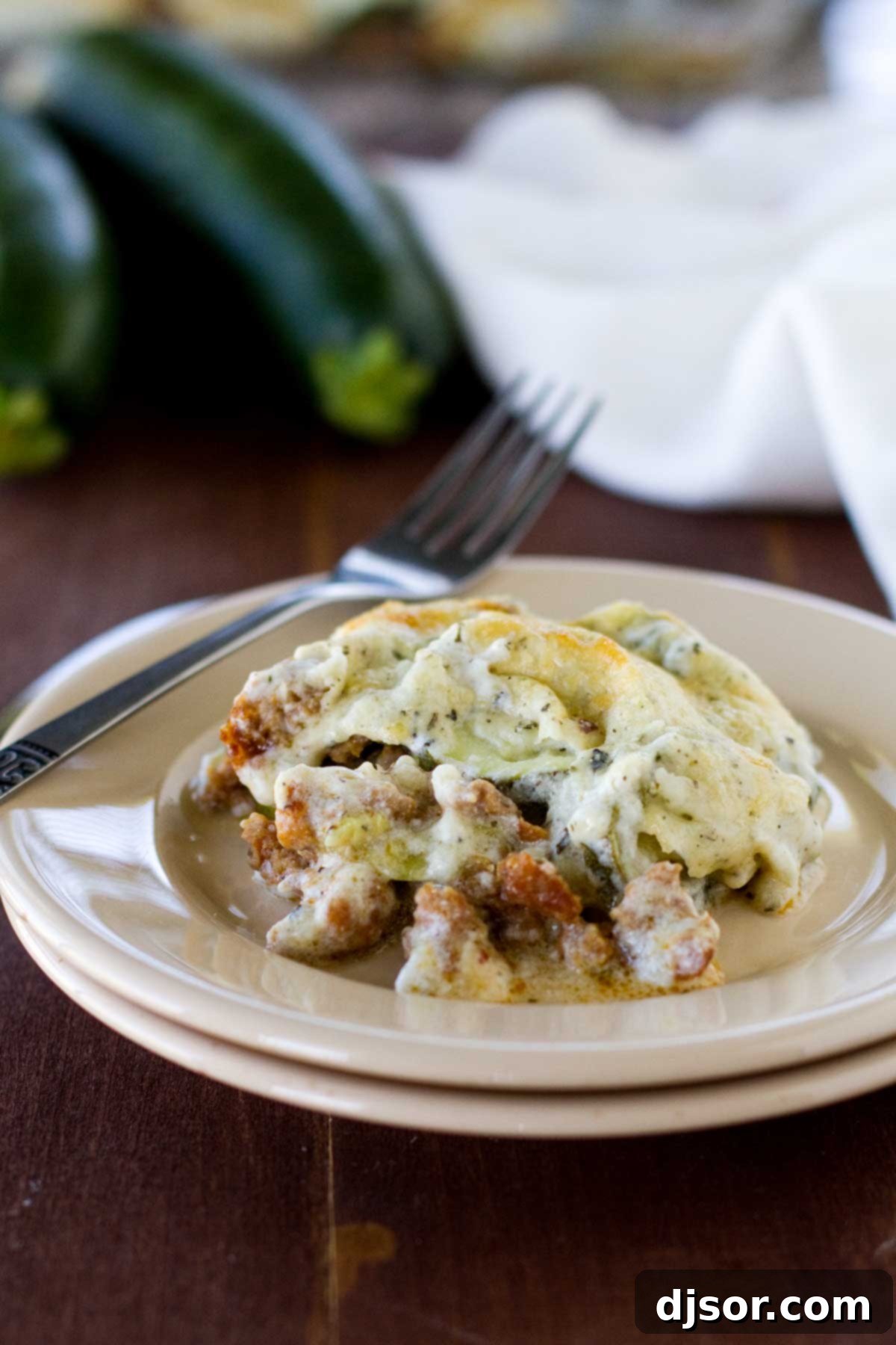 A generous serving of Zucchini Sausage Casserole on a white plate with a fork, showing the creamy sauce, tender zucchini, and savory sausage.