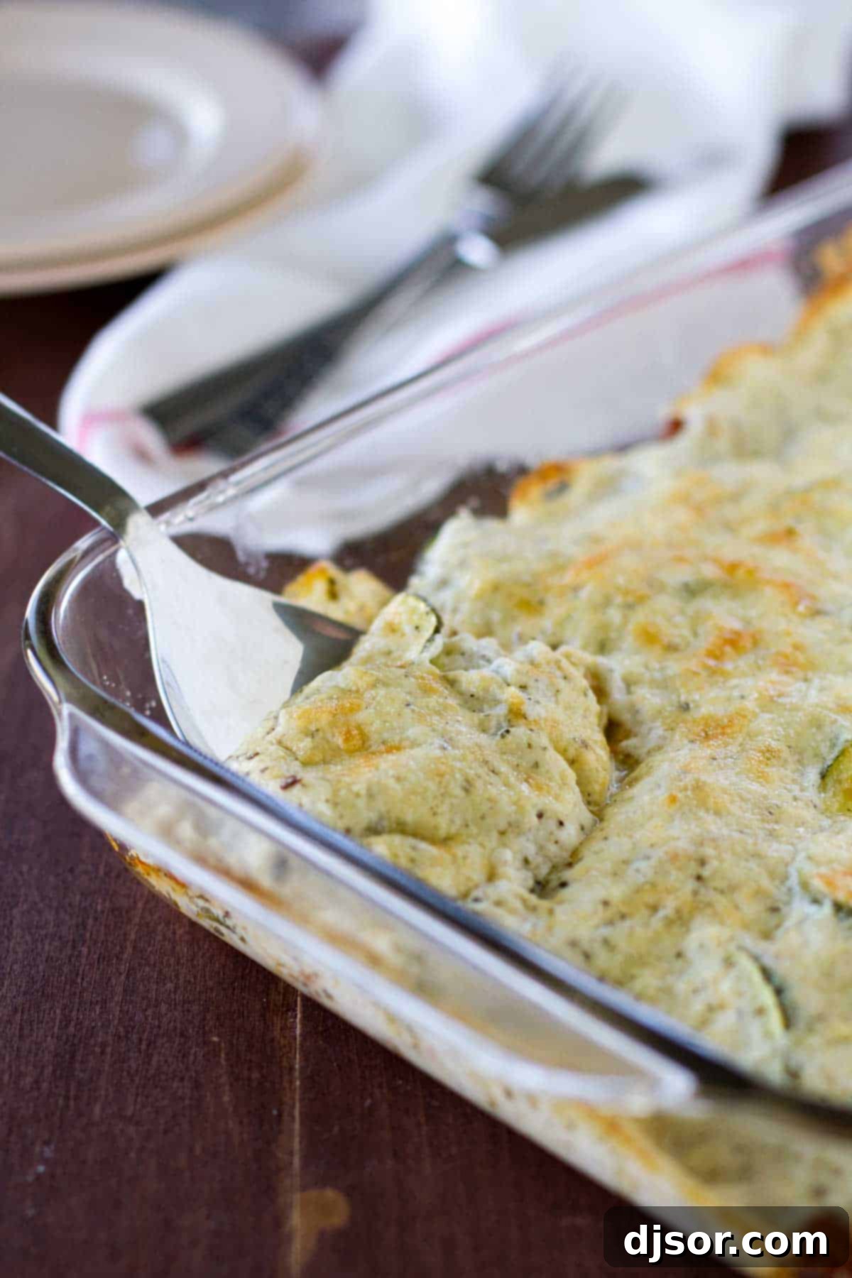 The baked Zucchini Sausage Casserole in a rectangular baking dish, with a serving spoon nestled in its creamy, bubbling contents.