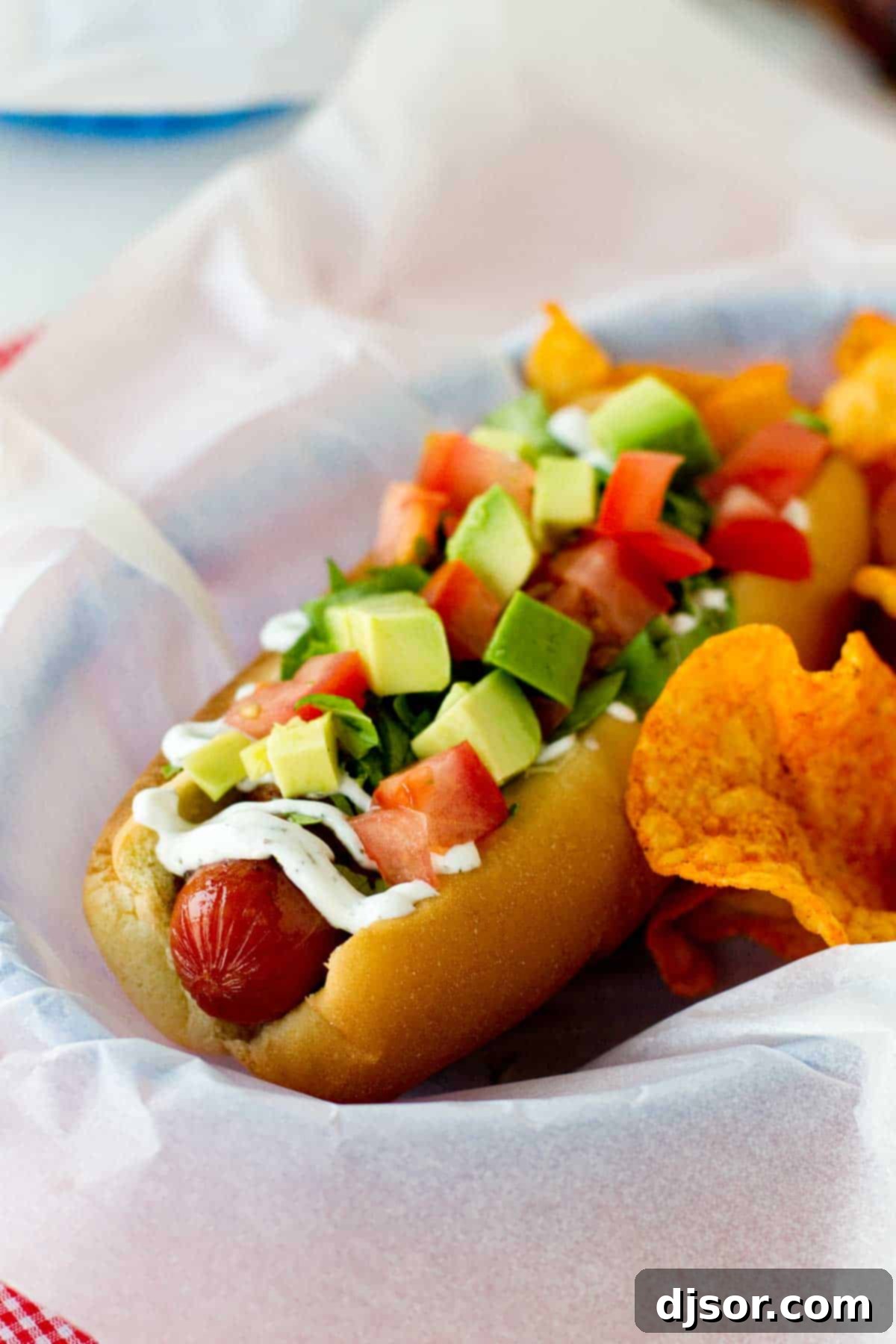 Bacon, lettuce, avocado, and tomato topped hot dog in a parchment paper lined basket.