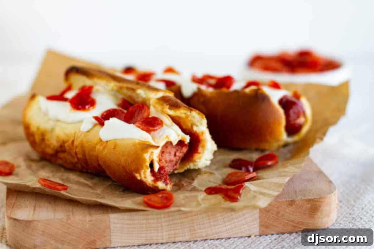 Delicious Pizza Hot Dog with a Bite Taken Pizza dogs on a cutting board with a bite taken from one of them, showcasing the melted cheese and pepperoni.