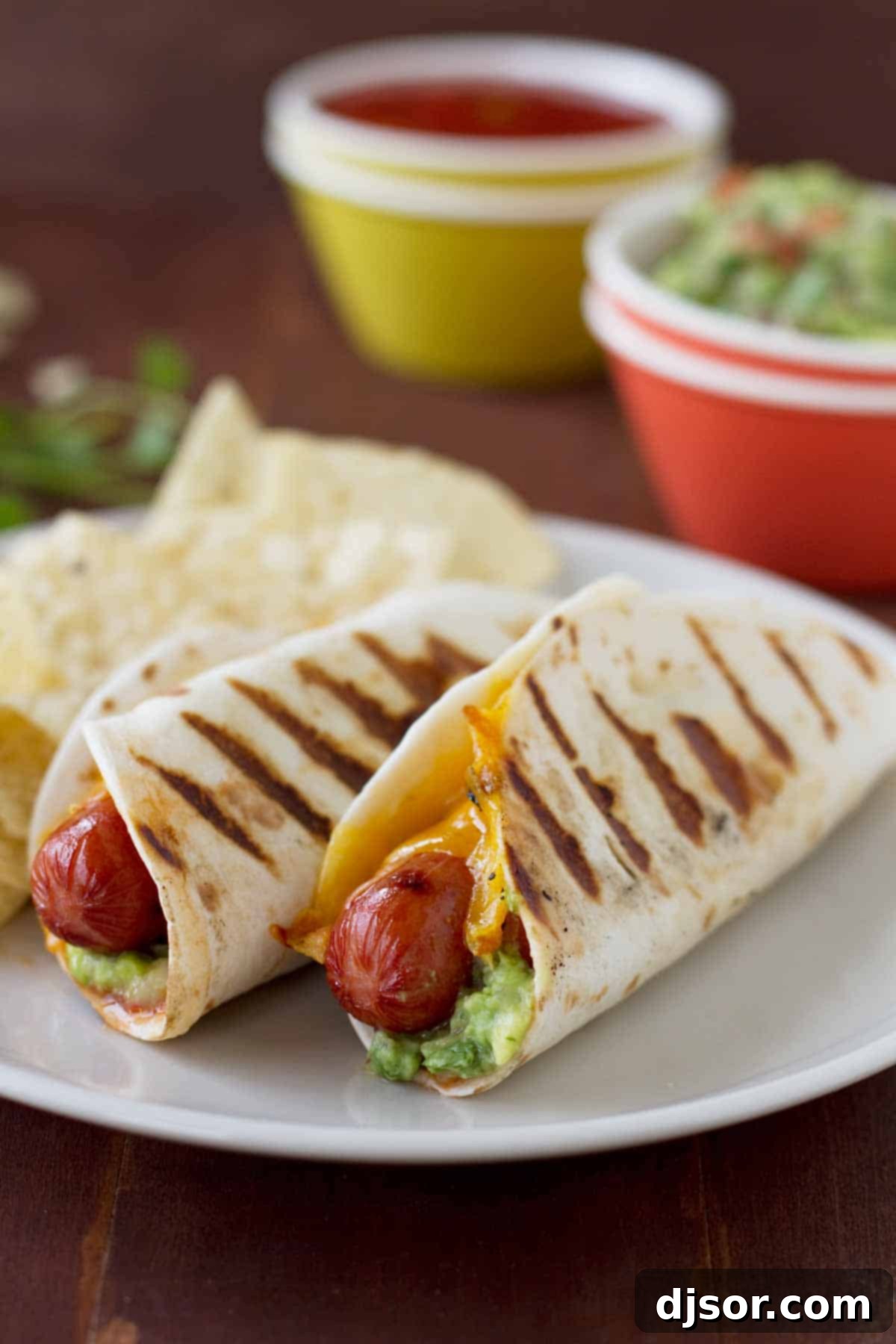 Taco Dogs - Hot dogs go Mexican with these hot dogs that are topped with guacamole and salsa and wrapped in a flour tortilla. Two Taco Dogs on a plate - hot dogs wrapped in a tortilla and grilled