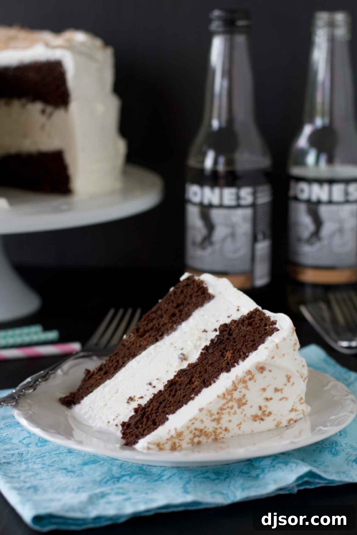 A perfectly sliced Root Beer Float Ice Cream Cake on a white plate, showcasing its distinct layers of cake and creamy vanilla ice cream. The cake is garnished with a hint of whipped cream and chocolate shavings.