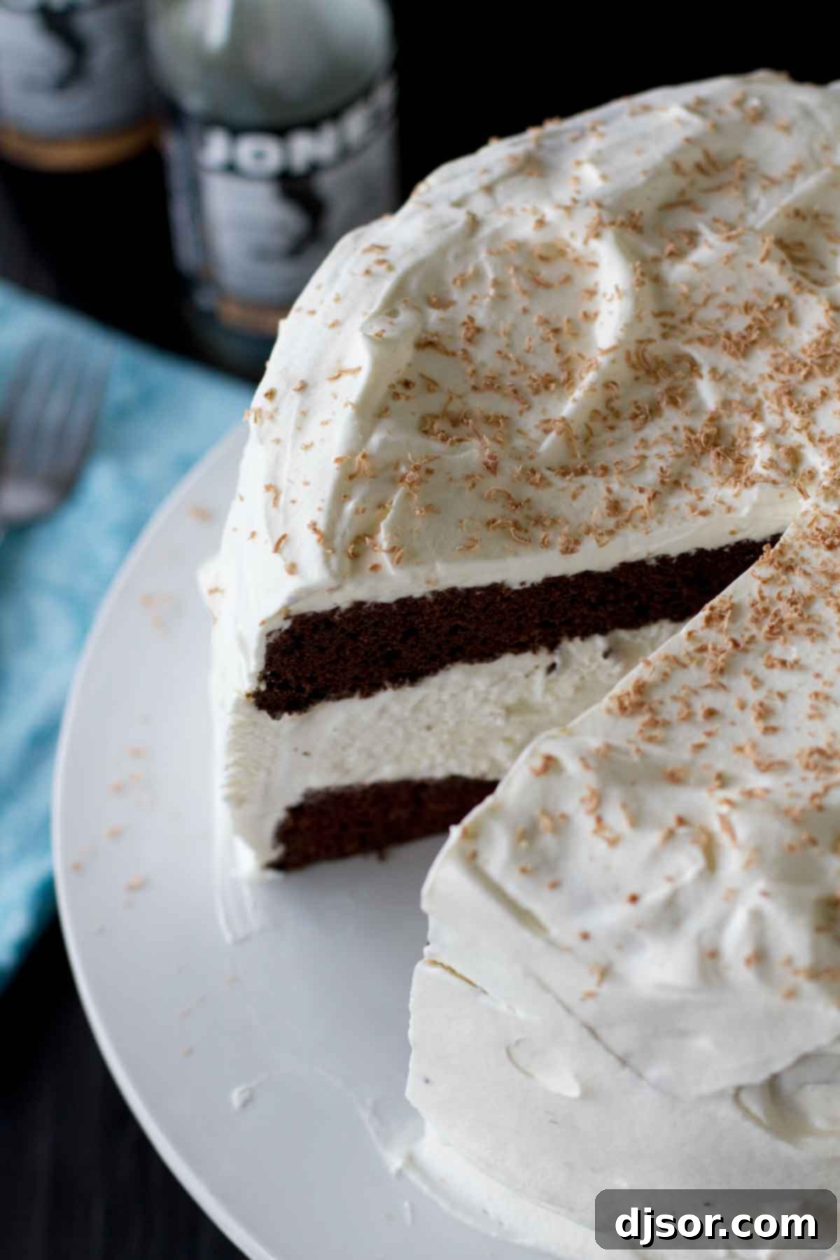 A complete Root Beer Float Ice Cream Cake with one slice removed, revealing the beautiful layers of dark root beer cake and white vanilla ice cream. The cake is topped with generous swirls of whipped cream, inviting a taste.