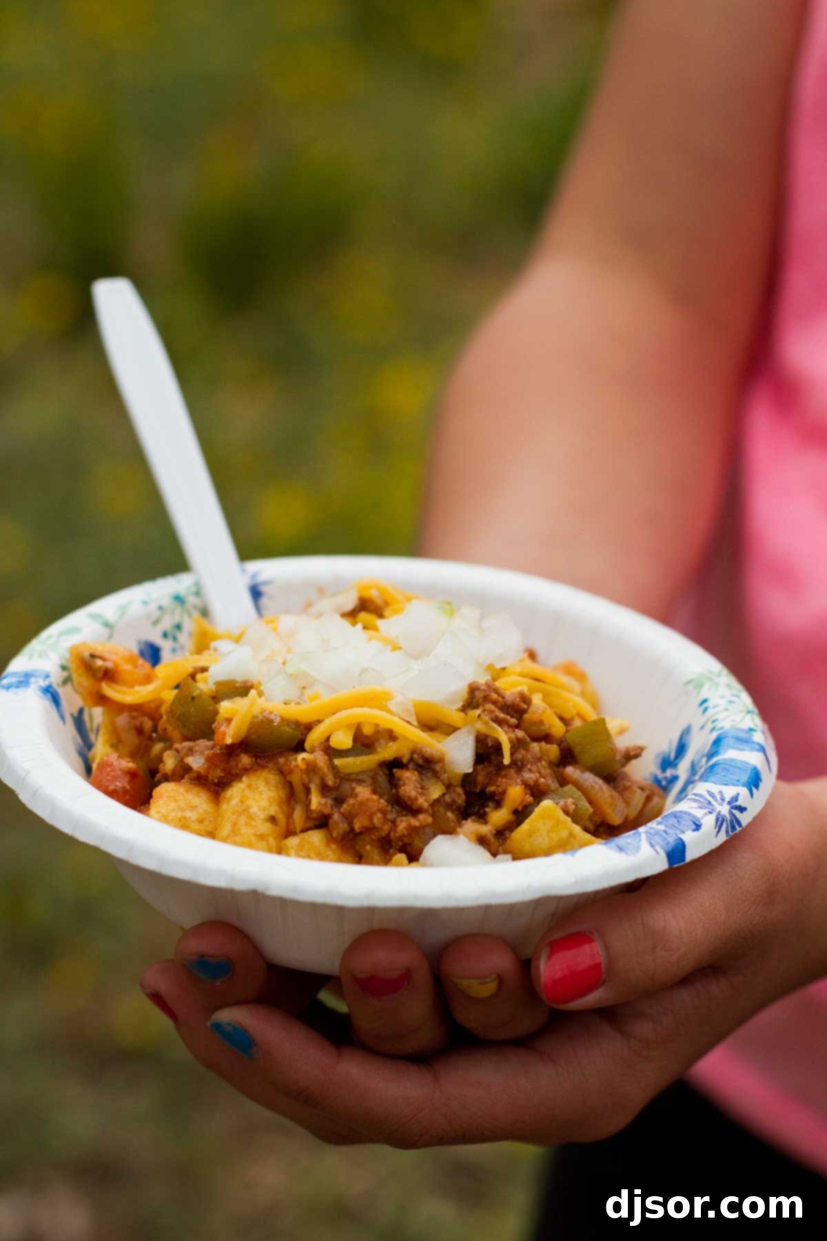 A comforting bowl of Dutch Oven Frito Pie, showcasing rich chili over Fritos with cheese and onions.