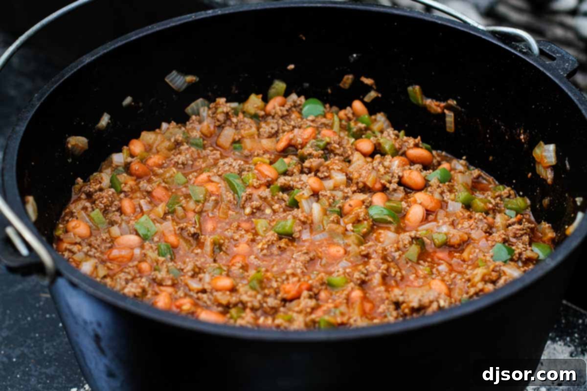A close-up shot of rich, simmering homemade chili in a Dutch oven, ready for Frito Pie assembly.