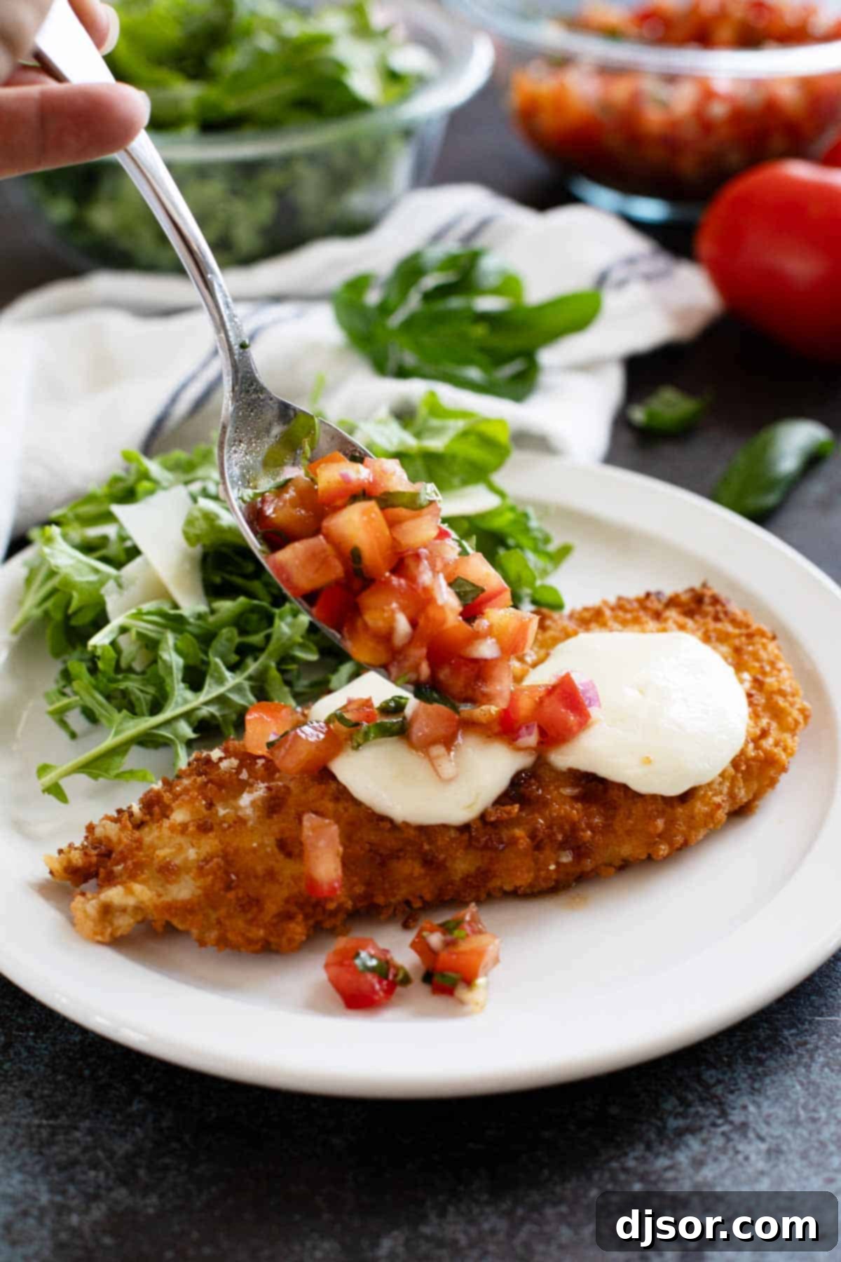 Freshly cooked Bruschetta Chicken pieces topped with melted mozzarella, being generously covered with the vibrant diced tomato and basil topping.