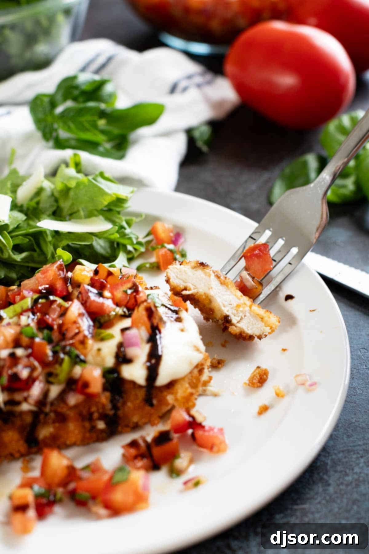 A close-up of Bruschetta Chicken on a plate, with a fork holding a bite-sized piece of chicken, showcasing the crispy breading, melted mozzarella, and fresh tomato topping.