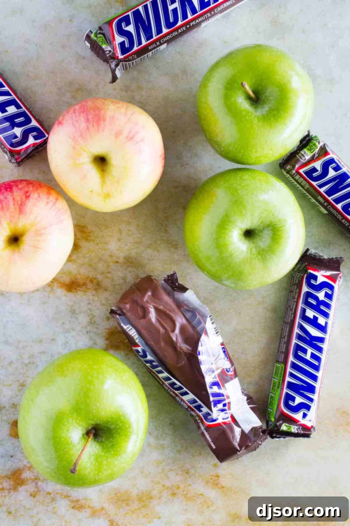 Ingredients for Snickers Salad laid out: instant vanilla pudding mix, milk, Cool Whip, chopped apples, chopped Snickers bars, grapes, and sliced strawberries.
