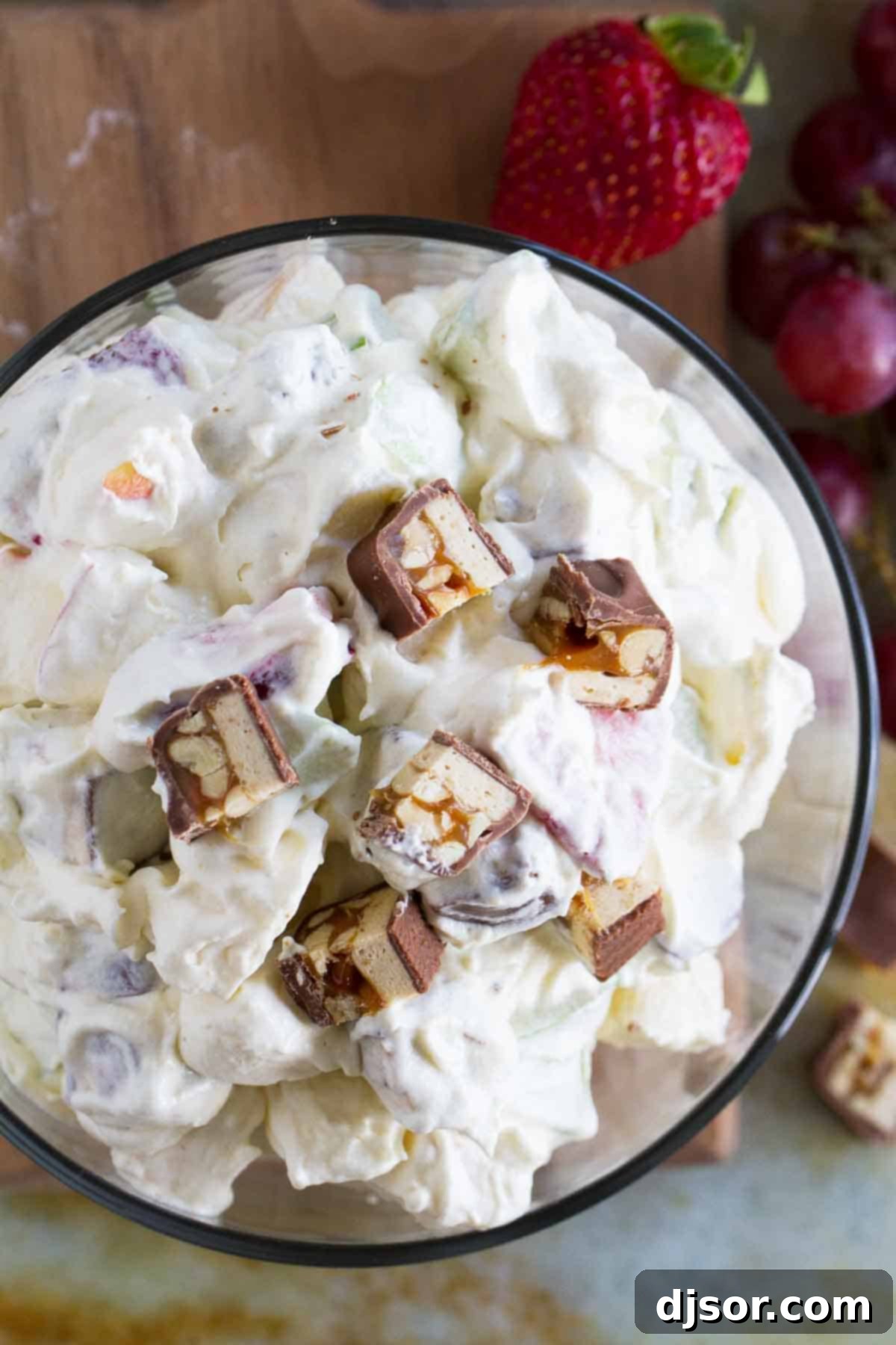 A large bowl of Snickers Apple Salad, garnished with extra chopped Snickers bars, showcasing the creamy texture, crisp apples, and colorful fruits.
