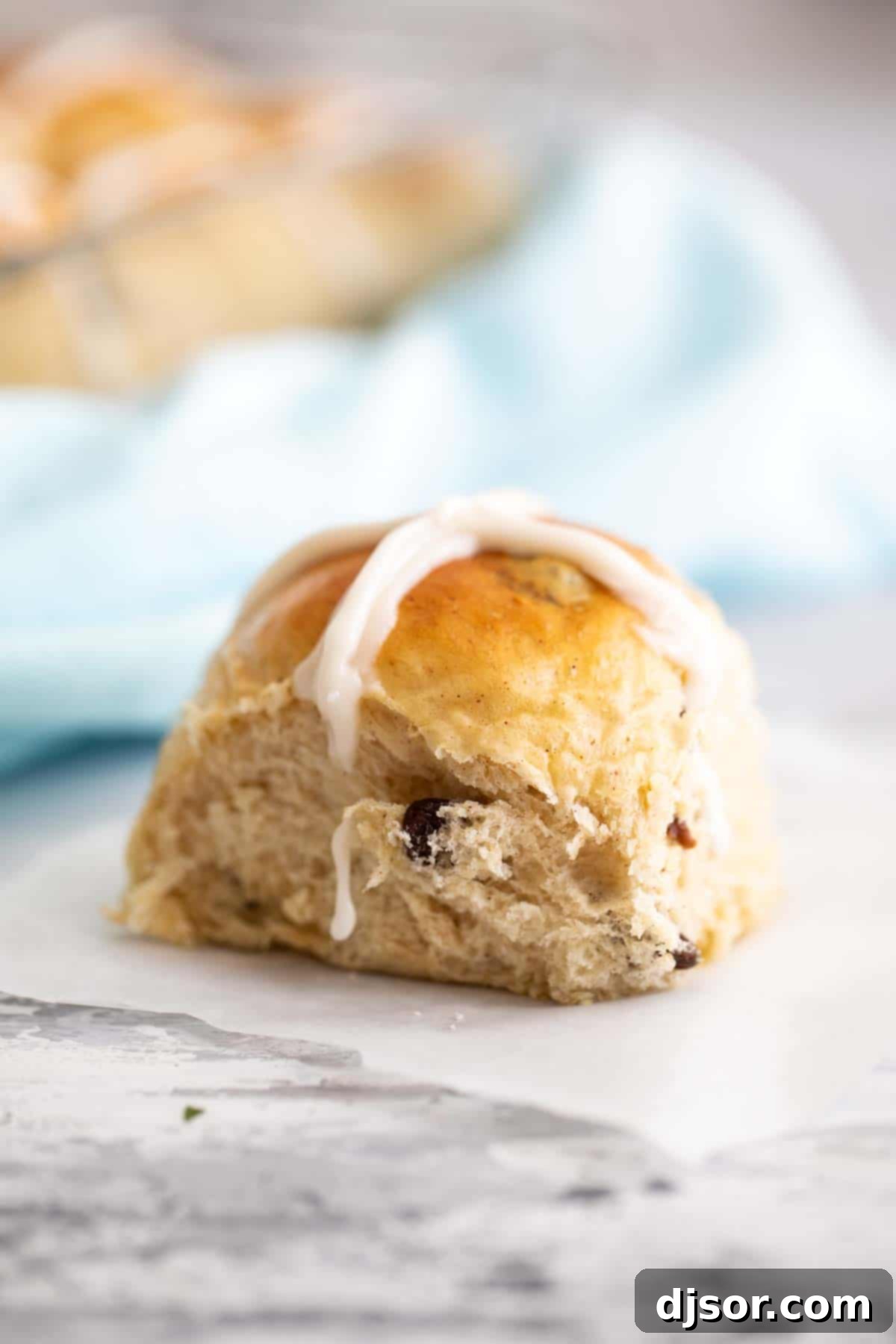 Perfectly Iced Hot Cross Bun A single Hot Cross Bun, perfectly baked with a glossy top and distinct icing cross, resting on parchment paper.