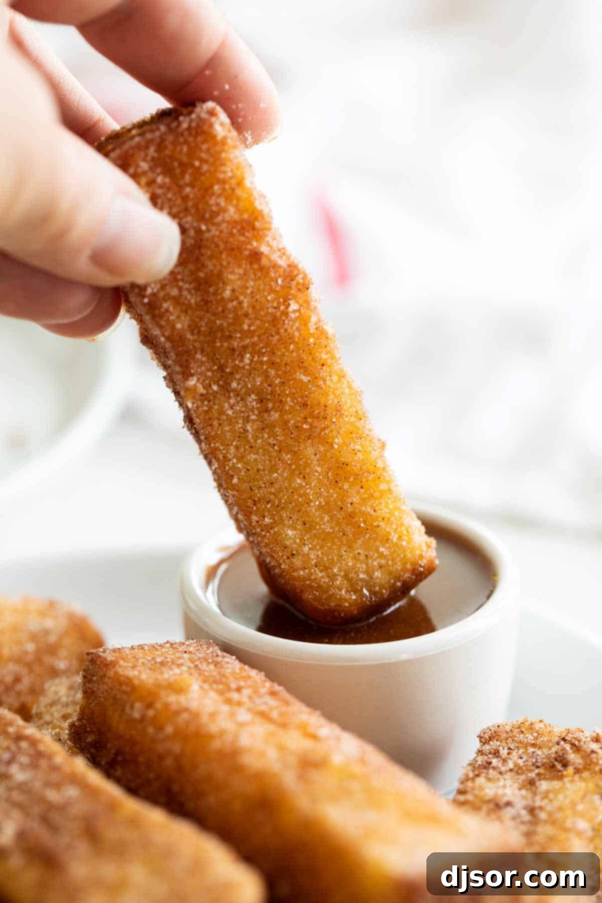 Spoil your family (or yourself!) for breakfast with these French Toast Sticks. Bread is coated in a batter and lightly fried, then covered in cinnamon sugar in this delicious breakfast treat. French Toast Sticks being dipped into a small bowl of creamy buttermilk syrup, ready to be enjoyed.