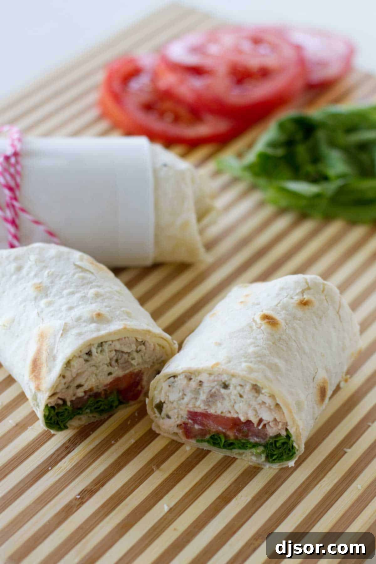 Close-up of a chicken pesto wrap with tomato and lettuce, neatly cut in half, revealing the layers of filling.