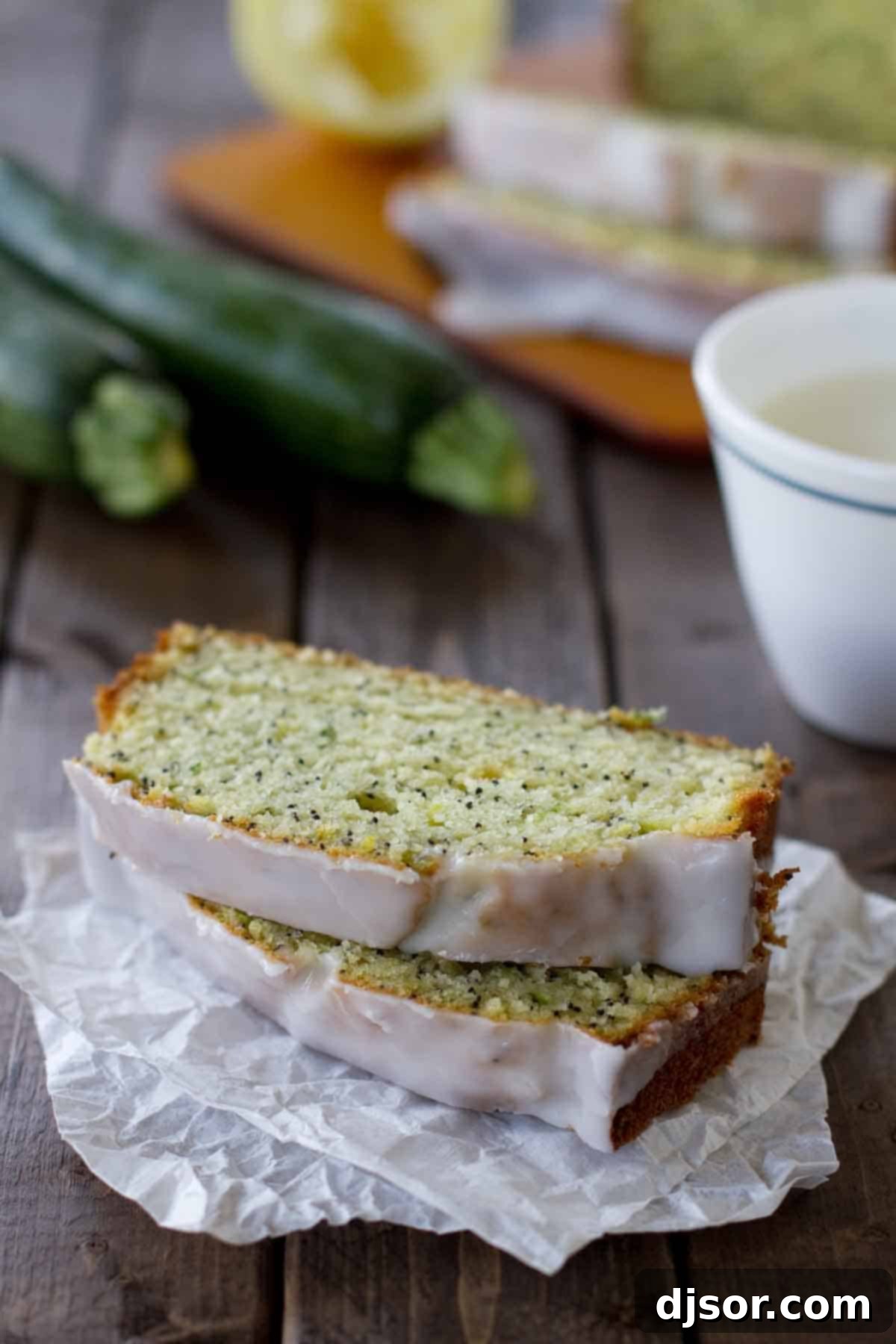 Two generous slices of Glazed Lemon Poppy Seed Zucchini Bread, perfectly moist and dotted with poppy seeds, resting on parchment paper with fresh zucchini in the background.
