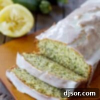 A freshly baked loaf of Glazed Lemon Poppy Seed Zucchini Bread on a wooden cutting board, with several slices already cut, revealing the moist interior and poppy seeds.