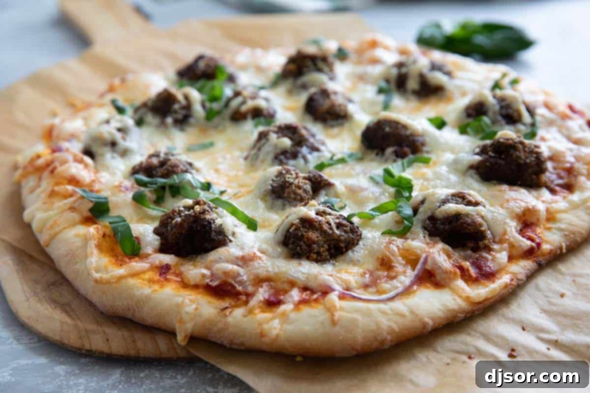 Comfort food at its finest – this Meatball Pizza is topped with homemade meatballs, onions and lots of cheese. Elevate your pizza night with this delicious recipe that will have everyone asking for seconds. A perfectly baked homemade meatball pizza, generously topped with savory meatballs, vibrant red onions, and melted mozzarella and parmesan cheese, garnished with fresh basil.