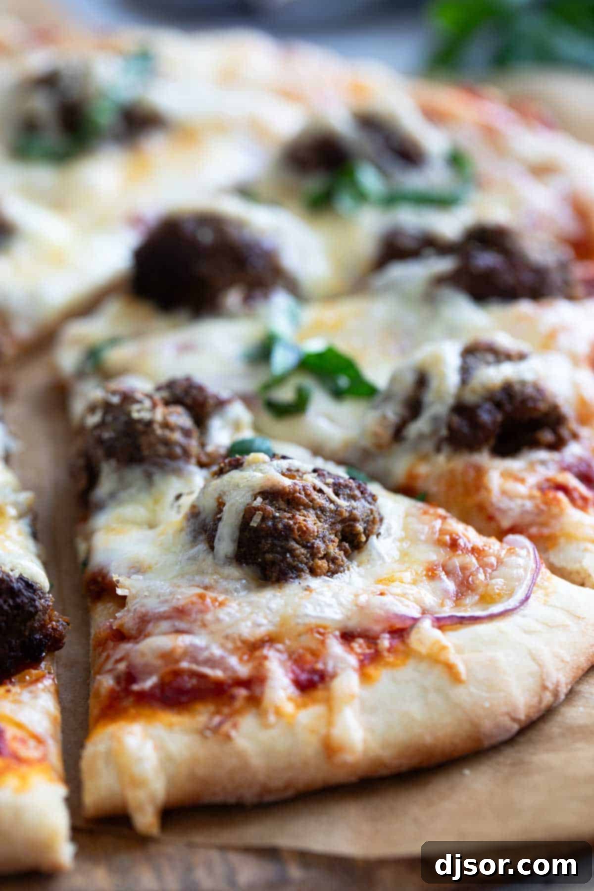 Comfort food at its finest – this Meatball Pizza is topped with homemade meatballs, onions and lots of cheese. Elevate your pizza night with this delicious recipe that will have everyone asking for seconds. A freshly baked meatball pizza, showcasing golden crust, bubbling melted cheese, savory halved meatballs, and caramelized red onions, ready to be sliced and served.