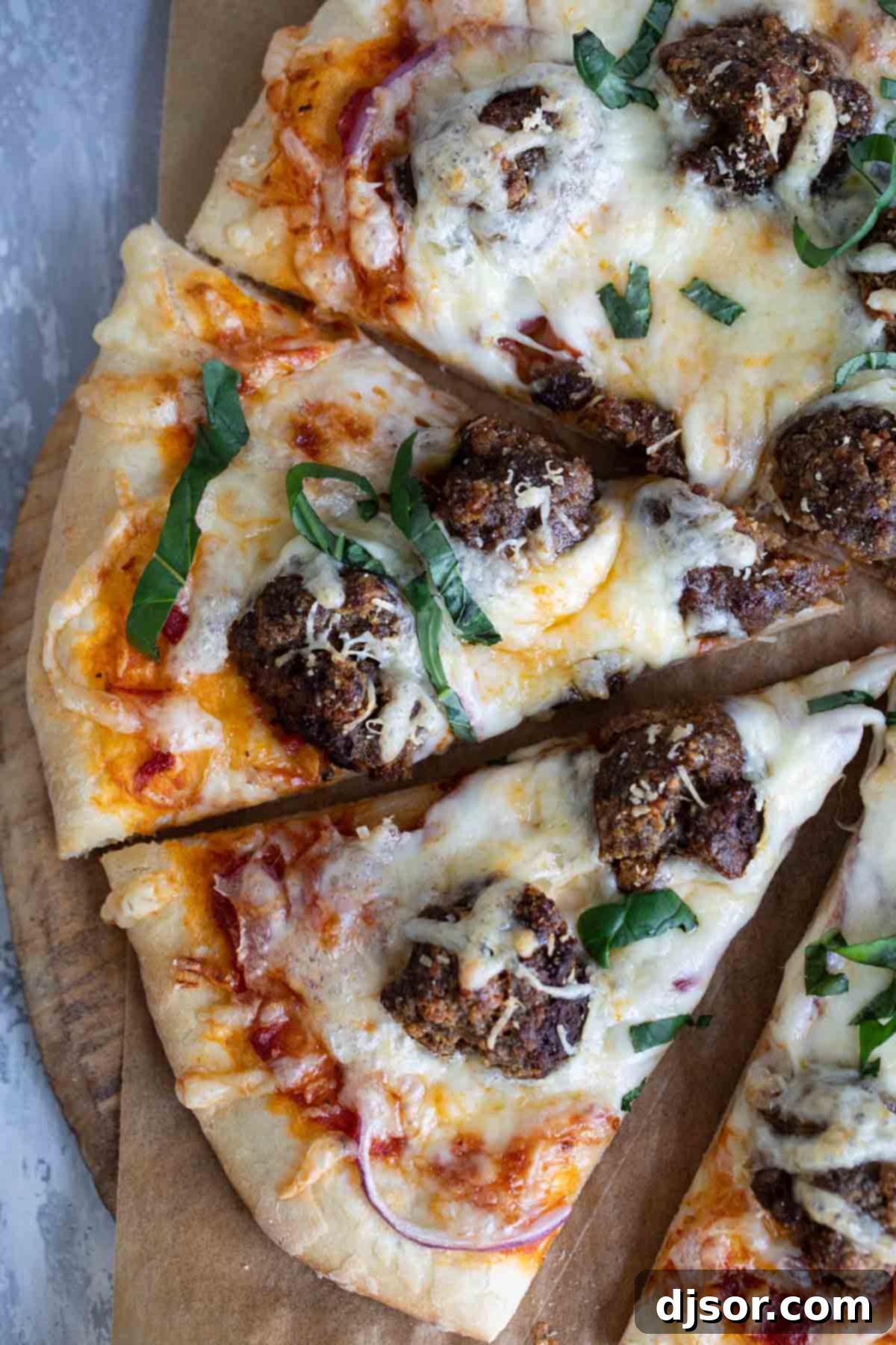 Comfort food at its finest – this Meatball Pizza is topped with homemade meatballs, onions and lots of cheese. Elevate your pizza night with this delicious recipe that will have everyone asking for seconds. A delicious meatball pizza, freshly cut into perfect slices, topped with vibrant green fresh basil, ready to be enjoyed as the ultimate comfort food.