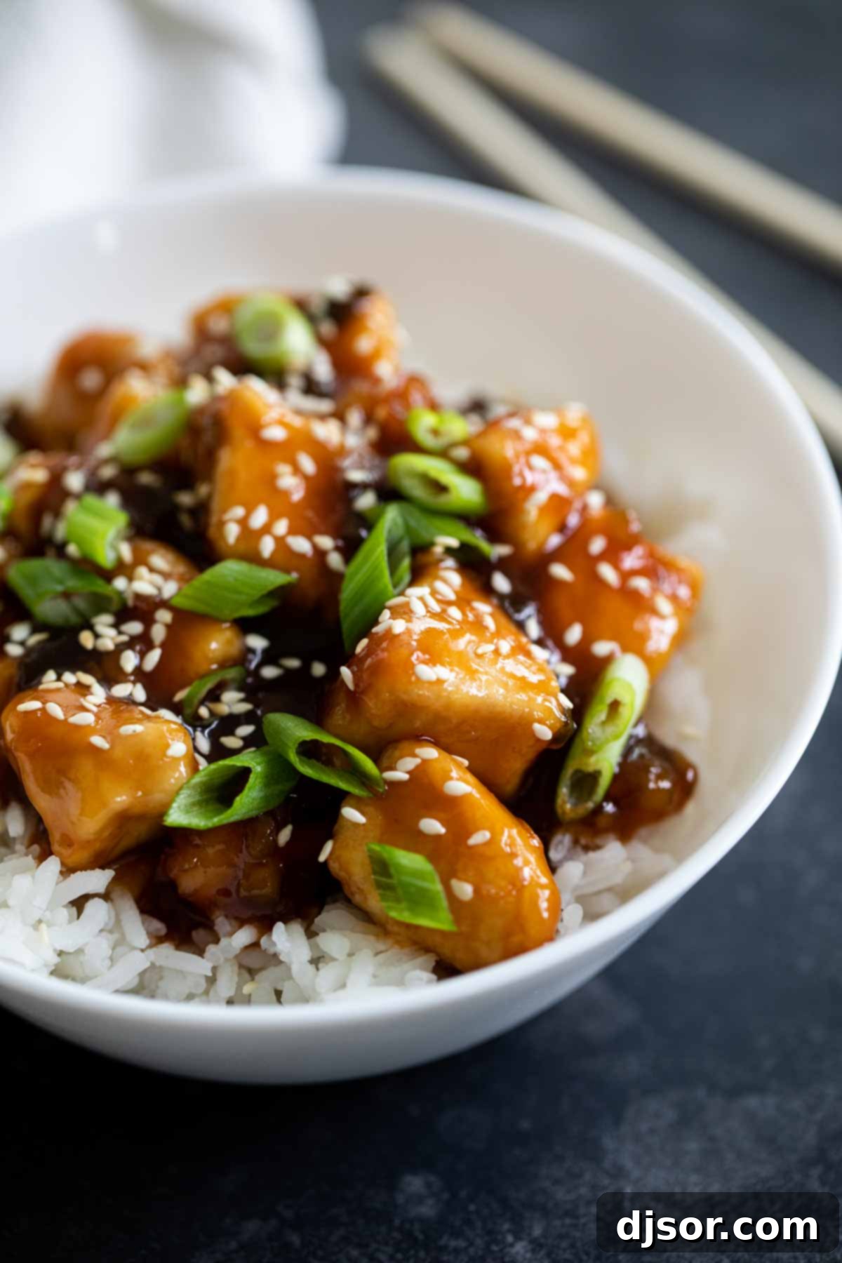 A vibrant bowl of homemade General Tso's Chicken, garnished with sesame seeds and fresh green onions, ready to be served over rice.