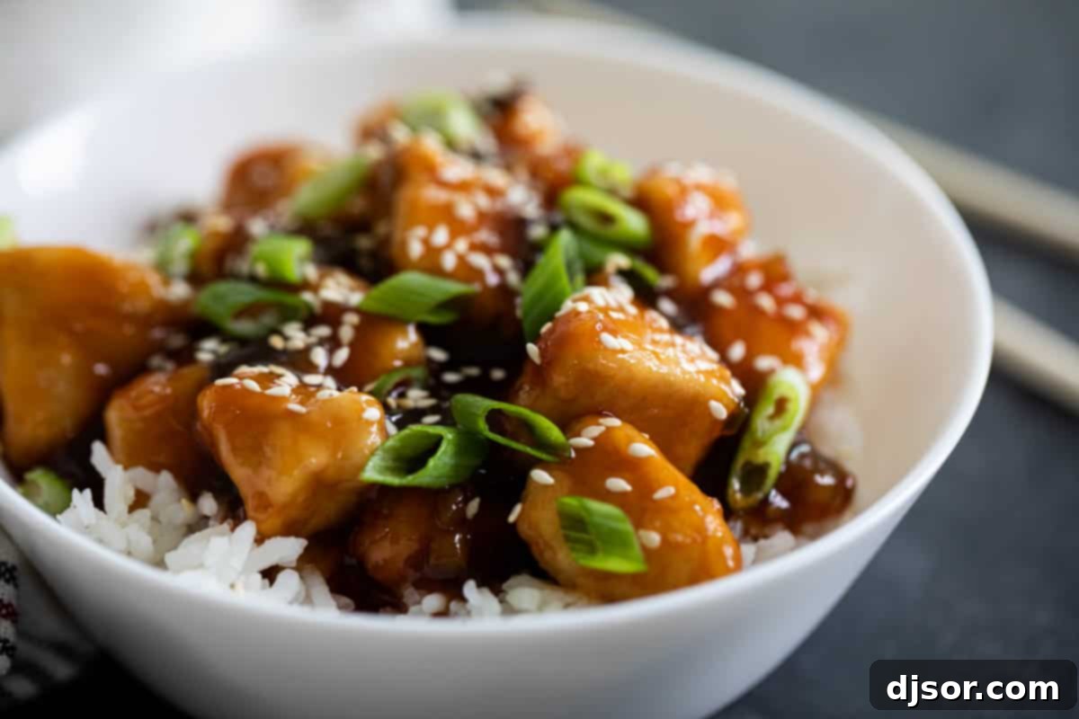 A beautifully plated dish of General Tso's Chicken served over fluffy white rice in a pristine white bowl, garnished with fresh green onions.