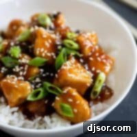 bowl filled with general tso chicken topped with sesame seeds and green onions