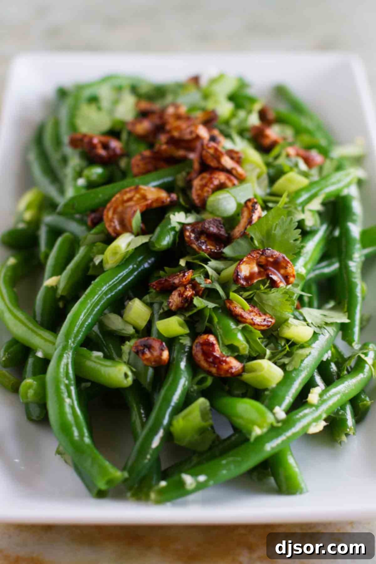 Vibrant Asian Green Bean Salad topped generously with golden, glistening soy-glazed cashews, showcasing fresh ingredients and a captivating texture.