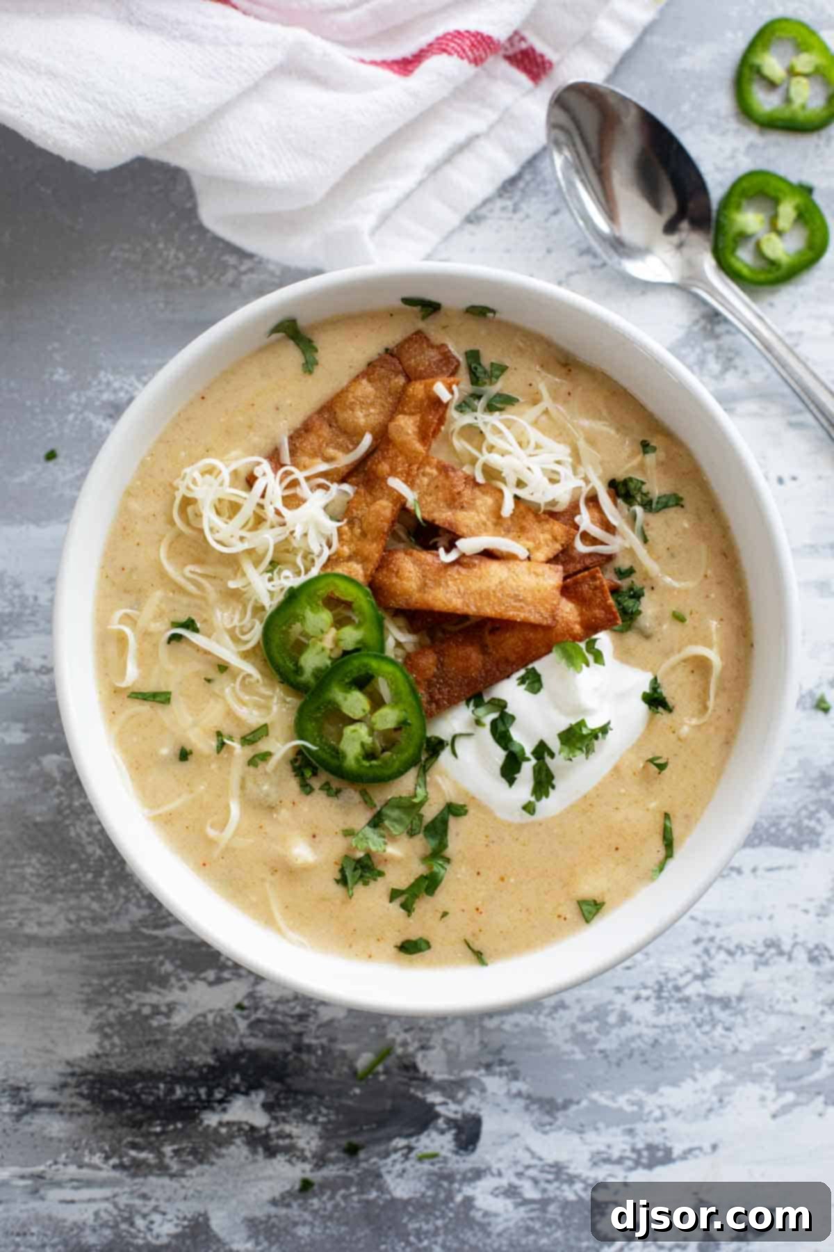 A beautifully garnished bowl of green chicken enchilada soup, adorned with crispy tortilla strips, fresh cilantro, cool sour cream, and spicy jalapeños.
