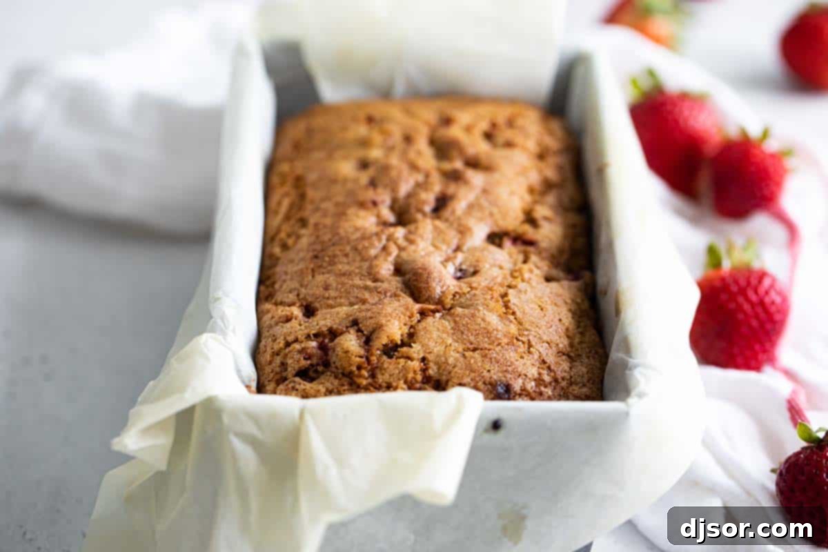 A freshly baked loaf of strawberry bread, golden brown and still in its baking pan, cooling on a wire rack.