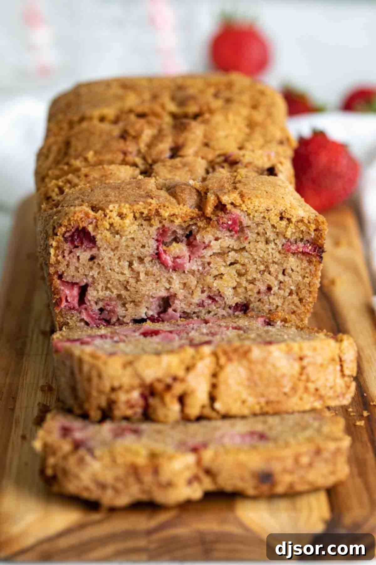 A whole loaf of golden-brown strawberry bread, freshly baked and sliced, resting on a rustic wooden cutting board, with visible chunks of strawberries.