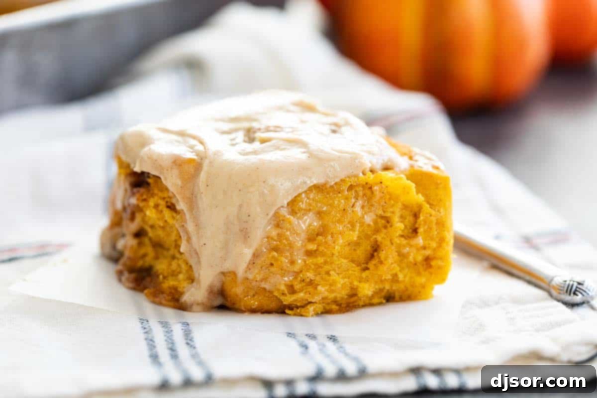 A single Pumpkin Cinnamon Roll with frosting generously dripping down its side, ready to be enjoyed.