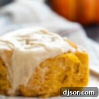 A delicious close-up of a single Pumpkin Cinnamon Roll, showcasing its fluffy texture and generous layer of maple cinnamon cream cheese frosting.