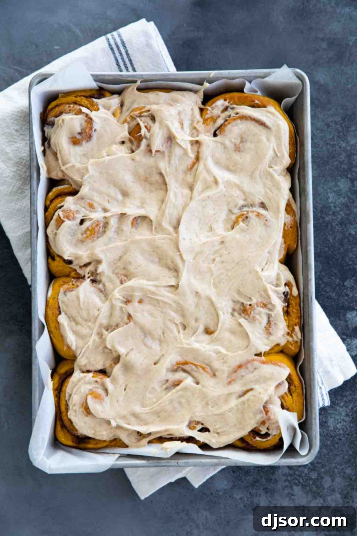 An overhead view of a pan brimming with freshly baked and generously frosted pumpkin cinnamon rolls, inviting you to take a bite.