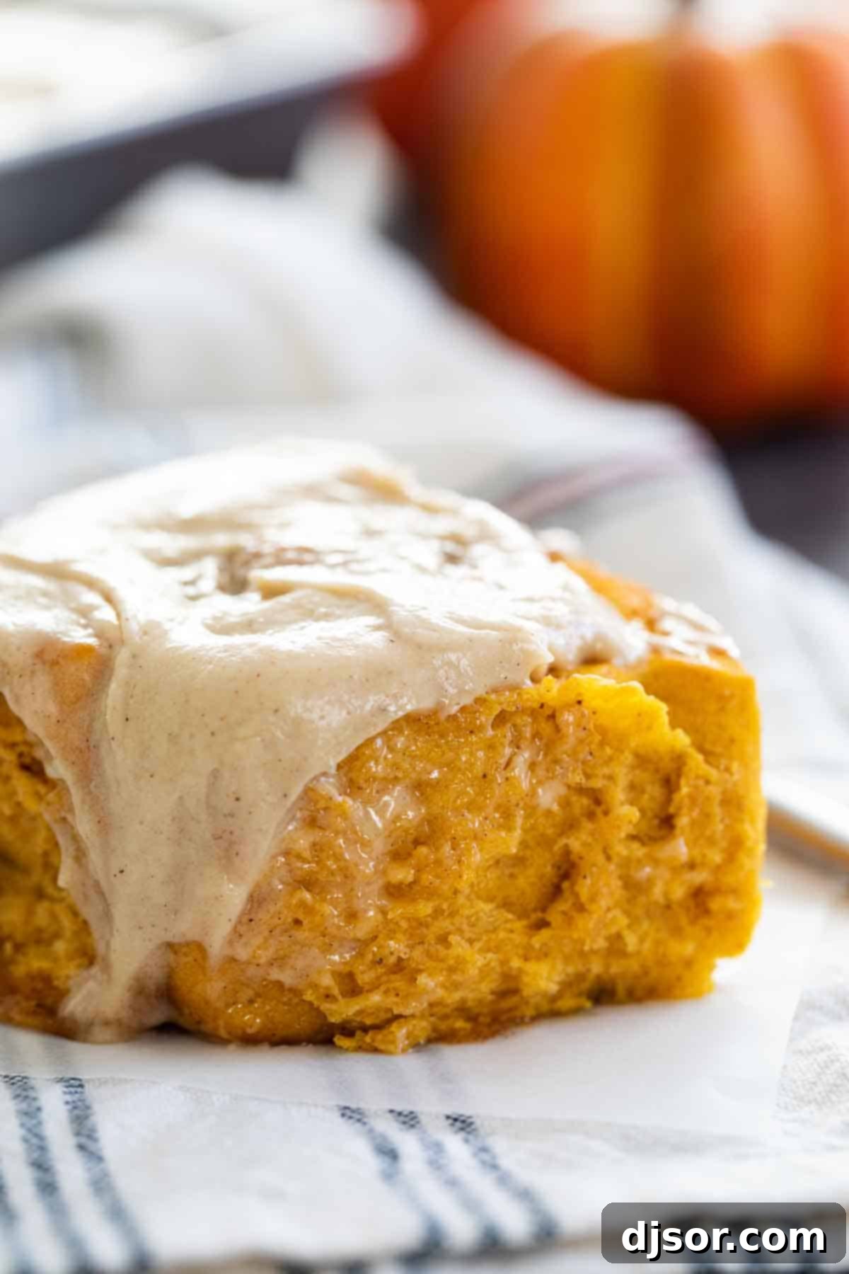 A mouthwatering close-up of a single Pumpkin Cinnamon Roll, showcasing its fluffy texture and generous layer of maple cinnamon cream cheese frosting.