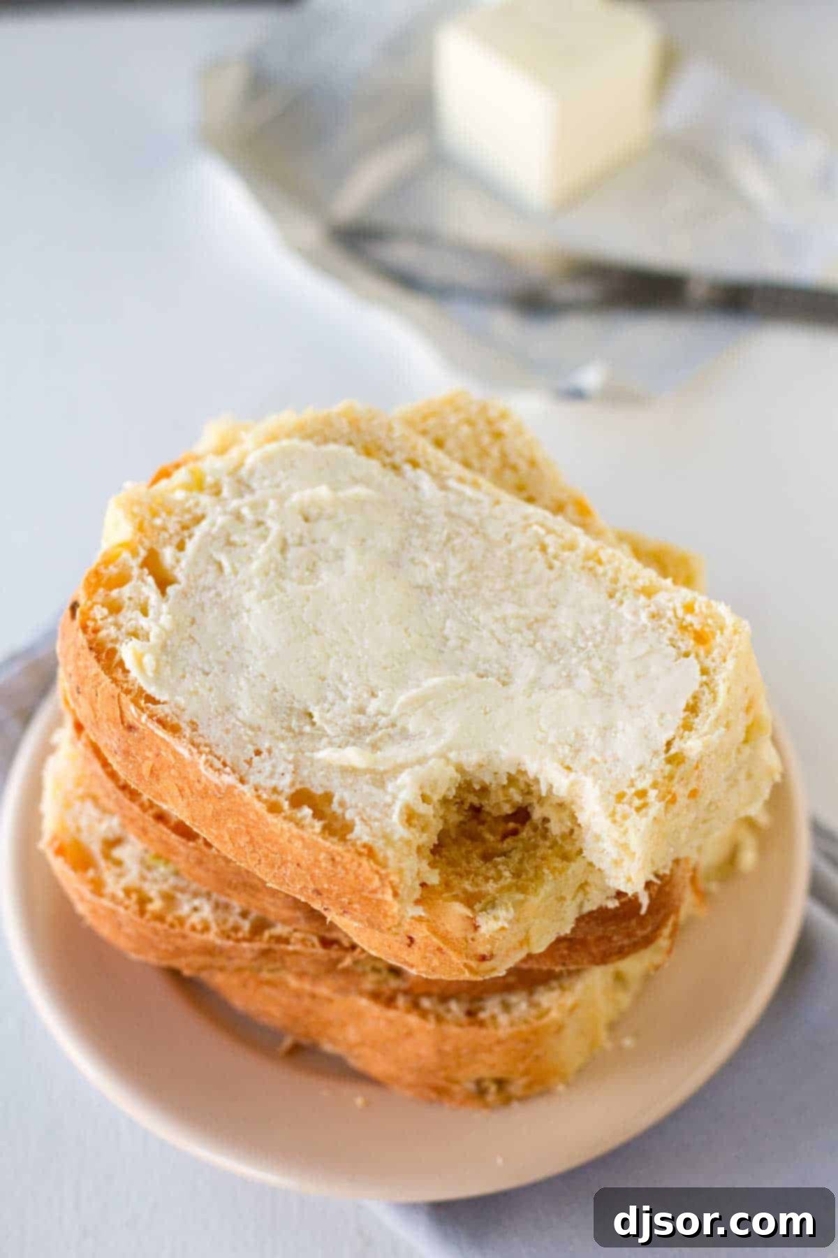 Several thick slices of Green Chile Cheddar Bread are stacked, with one slice showing a delightful bite taken from it, revealing the fluffy interior and specks of green chiles and melted cheddar.