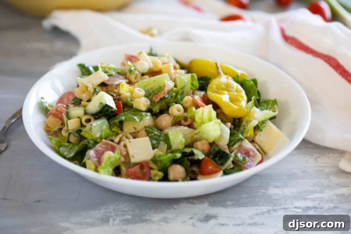 Hearty Italian Chopped Salad with Pepperoncini A large bowl of Italian Chopped Salad, generously topped with vibrant pepperoncini peppers, showcasing a mix of pasta, cured meats, and fresh vegetables.